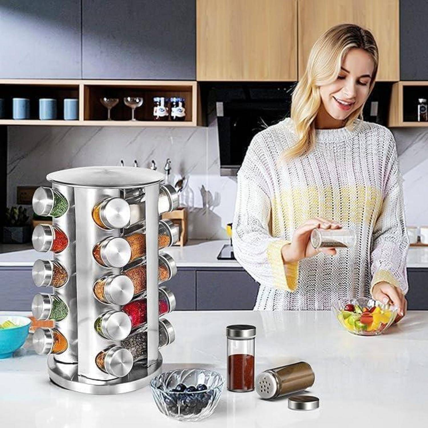 Frau, die Gewürze von einem rotierenden Edelstahl-Gewürzregal in einer modernen Küche verwendet, während sie eine Mahlzeit mit frischen Zutaten zubereitet.