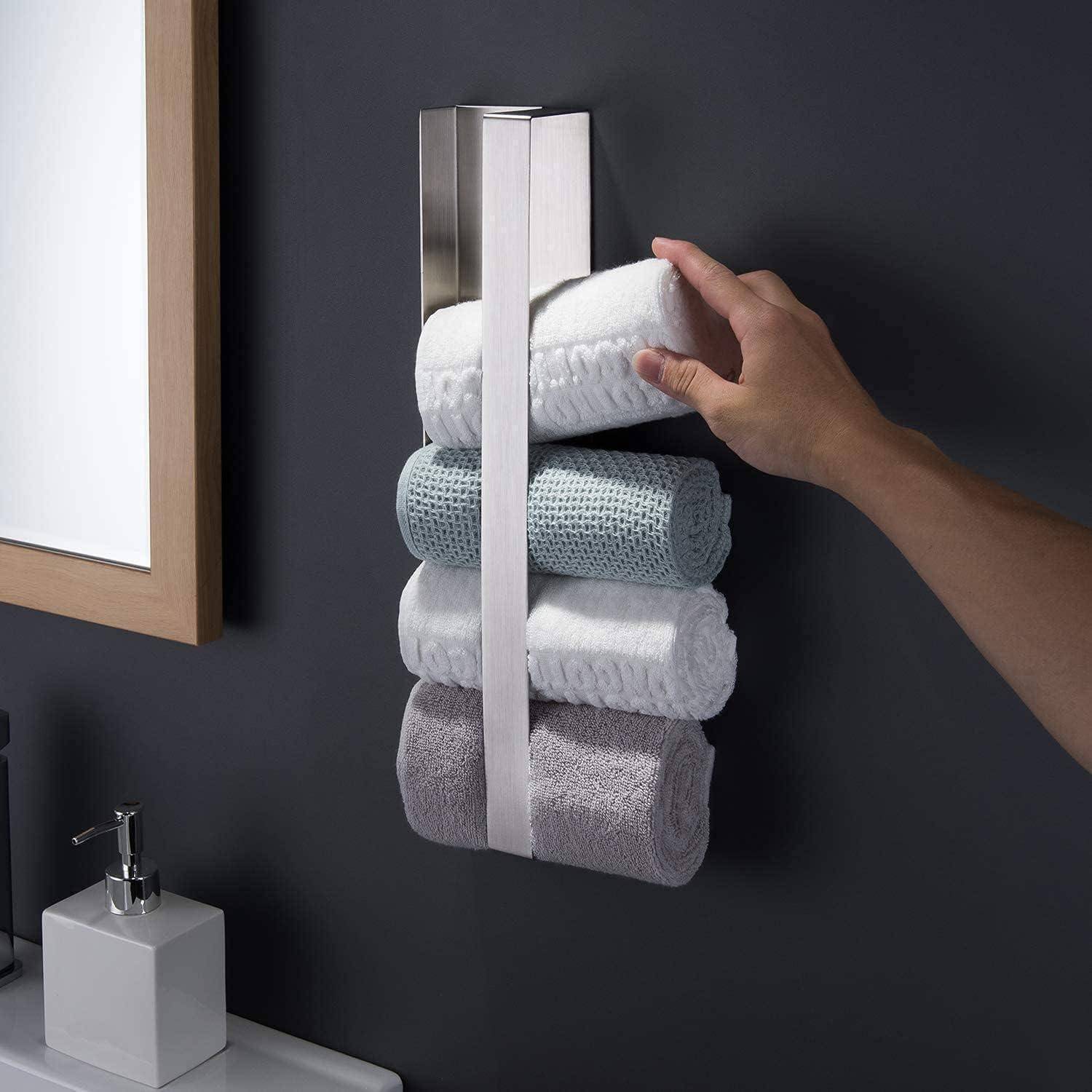 Eine Hand greift, um gerollte Handtücher auf einem modernen, vertikalen Handtuchhalter zu stapeln, der an einer dunklen Wand neben einem Spiegel und Waschbereich montiert ist.