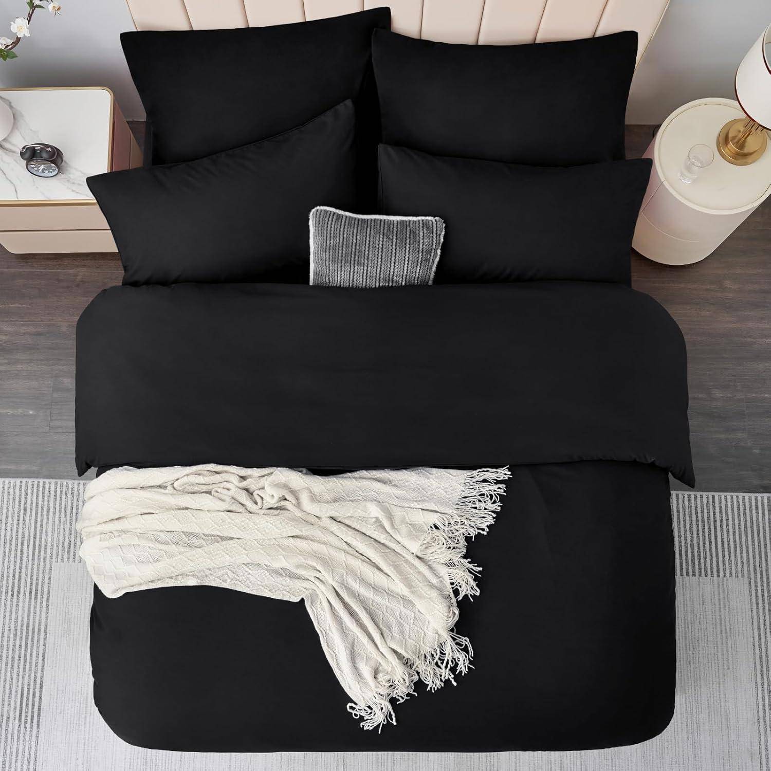 Ein ordentlich gemachtes Bett mit schwarzer Bettwäsche, einem kleinen Zierkissen und einer hellgefärbten Decke. Daneben steht ein Nachttisch mit einer Lampe.