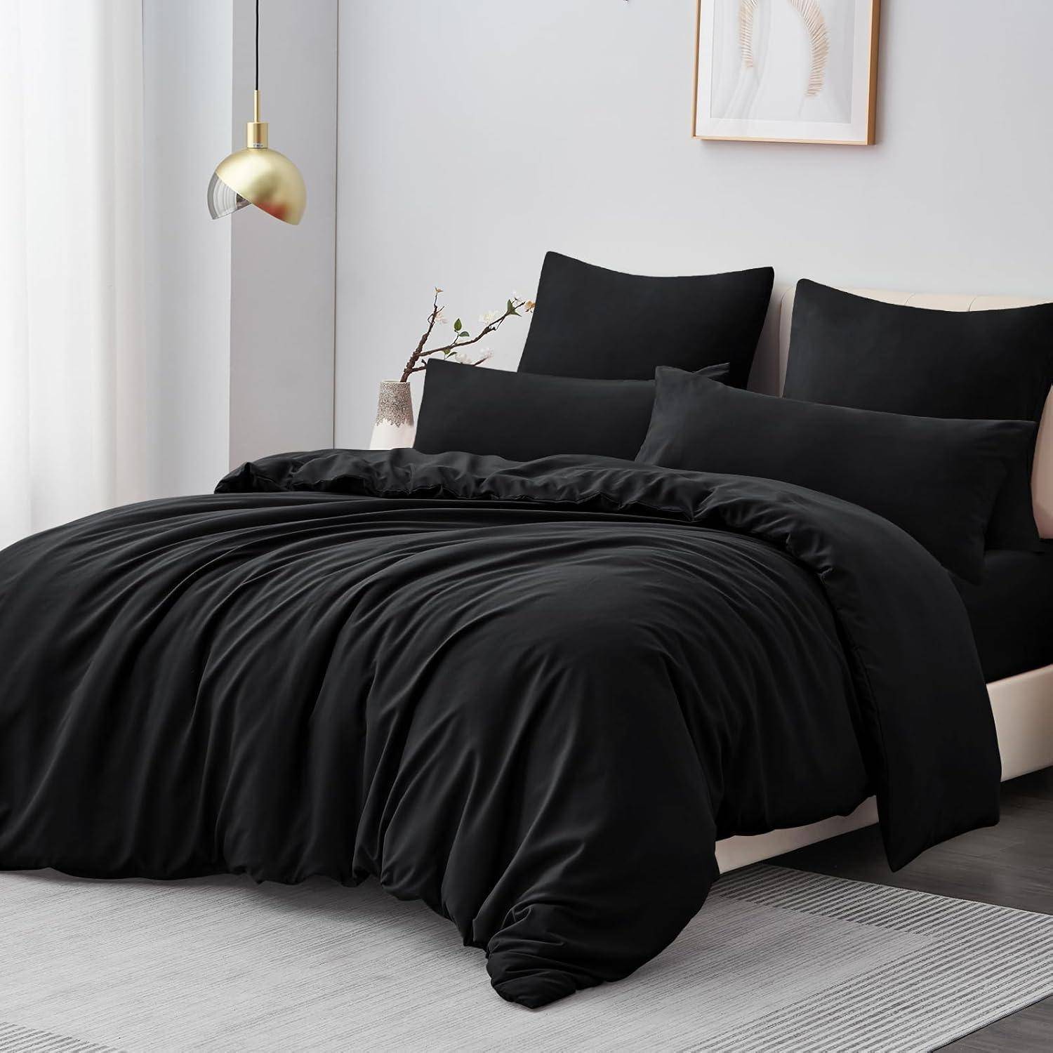 Ein Schlafzimmer zeigt ein ordentlich gemachtes Bett mit einer schwarzen Bettdecke und Kissen, eine moderne Lampe auf einem Beistelltisch und minimalistische Wandkunst.