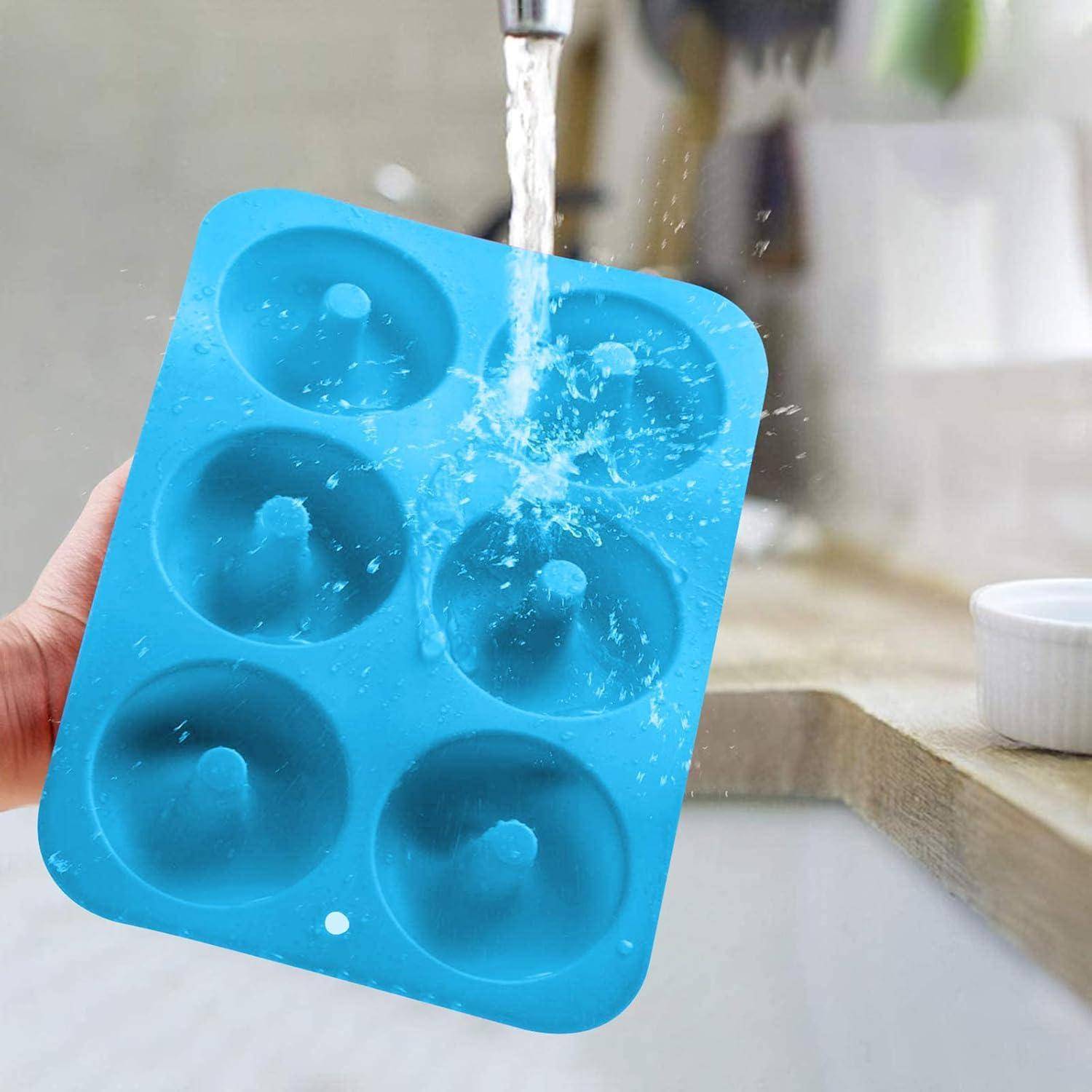 Eine blaue Silikondonutform, über die Wasser von einem Wasserhahn läuft, gehalten von einer Person über einem Küchenbecken.