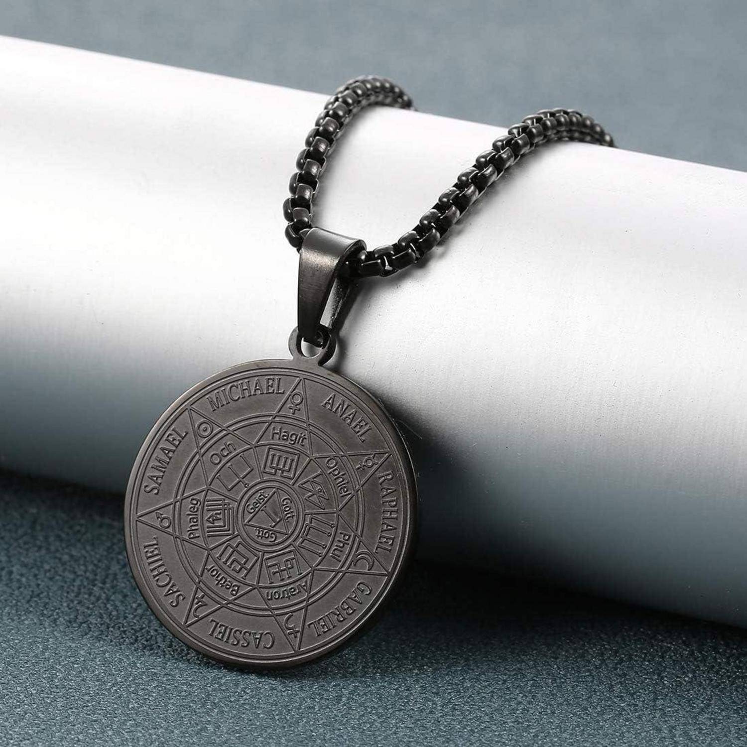 Ein runder Metallanhänger mit einer Kette, graviert mit Namen und Symbolen von Engeln. Der Anhänger hat einen dunklen, polierten Finish auf einem neutralen Hintergrund.