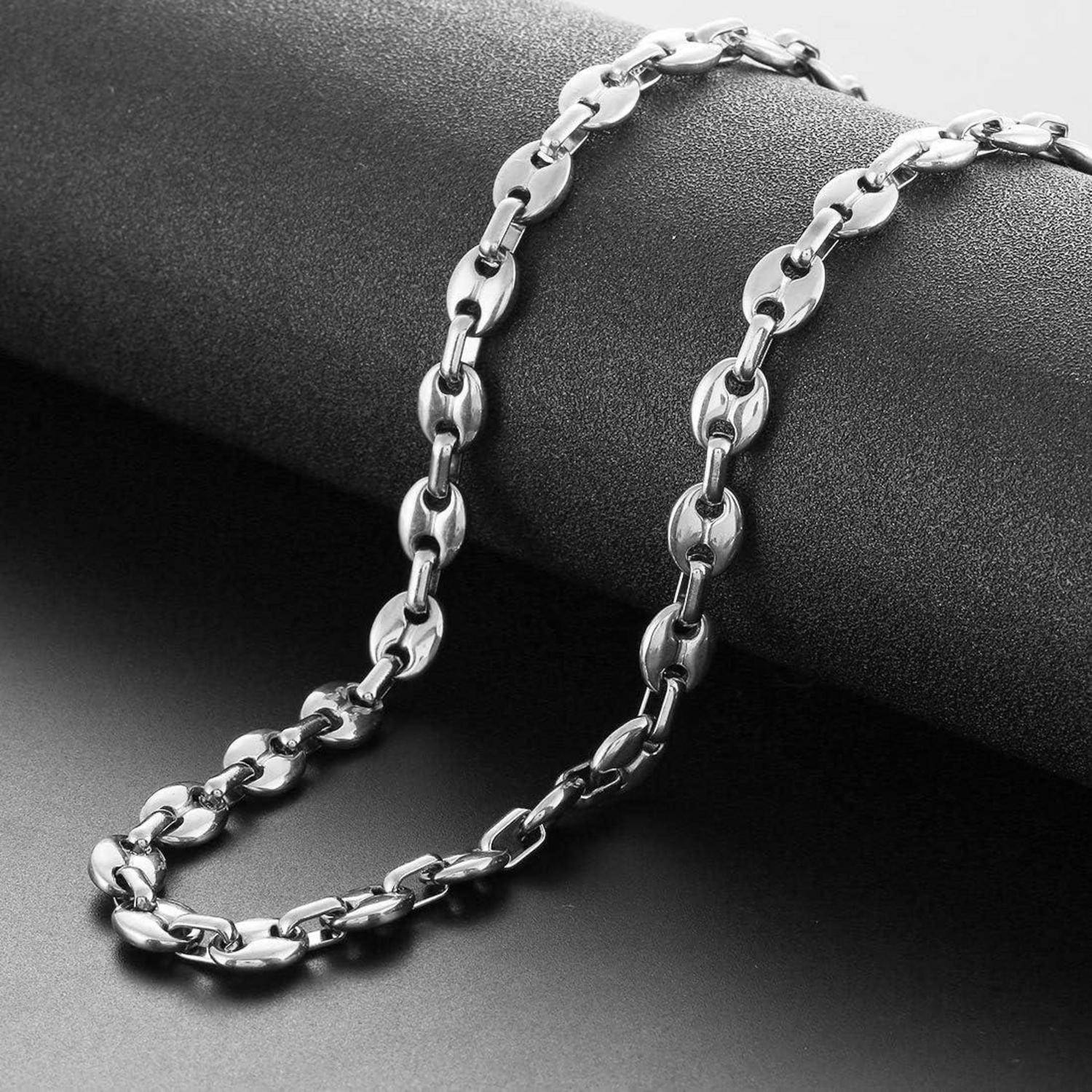 Eine Silberkette mit rechteckigen Gliedern, die über eine dunkle, strukturierte Oberfläche drapiert ist und ihren glatten, glänzenden Finish und ihr modernes Design zur Geltung bringt.