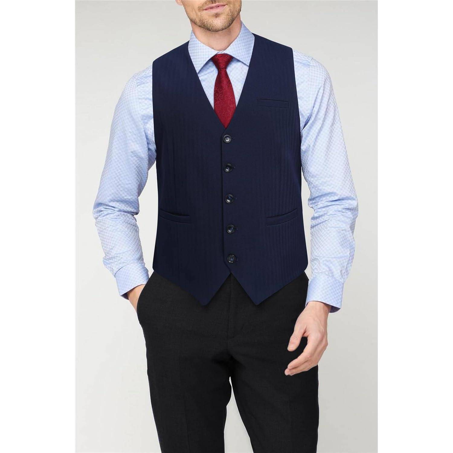Mann trägt eine blaue Weste, ein hellblaues gemustertes Hemd, eine rote Krawatte und schwarze Hosen und steht vor einem einfarbigen Hintergrund.