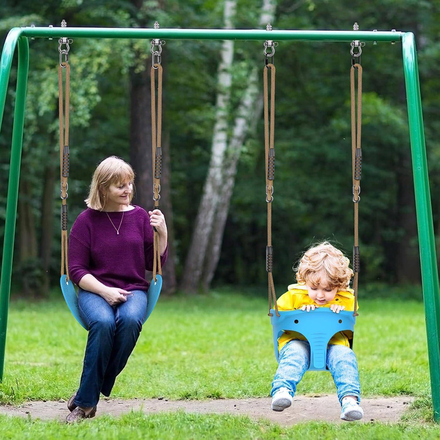 Eine Frau sitzt auf einer Schaukel neben einem Kind auf einem Spielplatz. Das Kind schaukelt sanft, umgeben von grünem Gras und Bäumen.