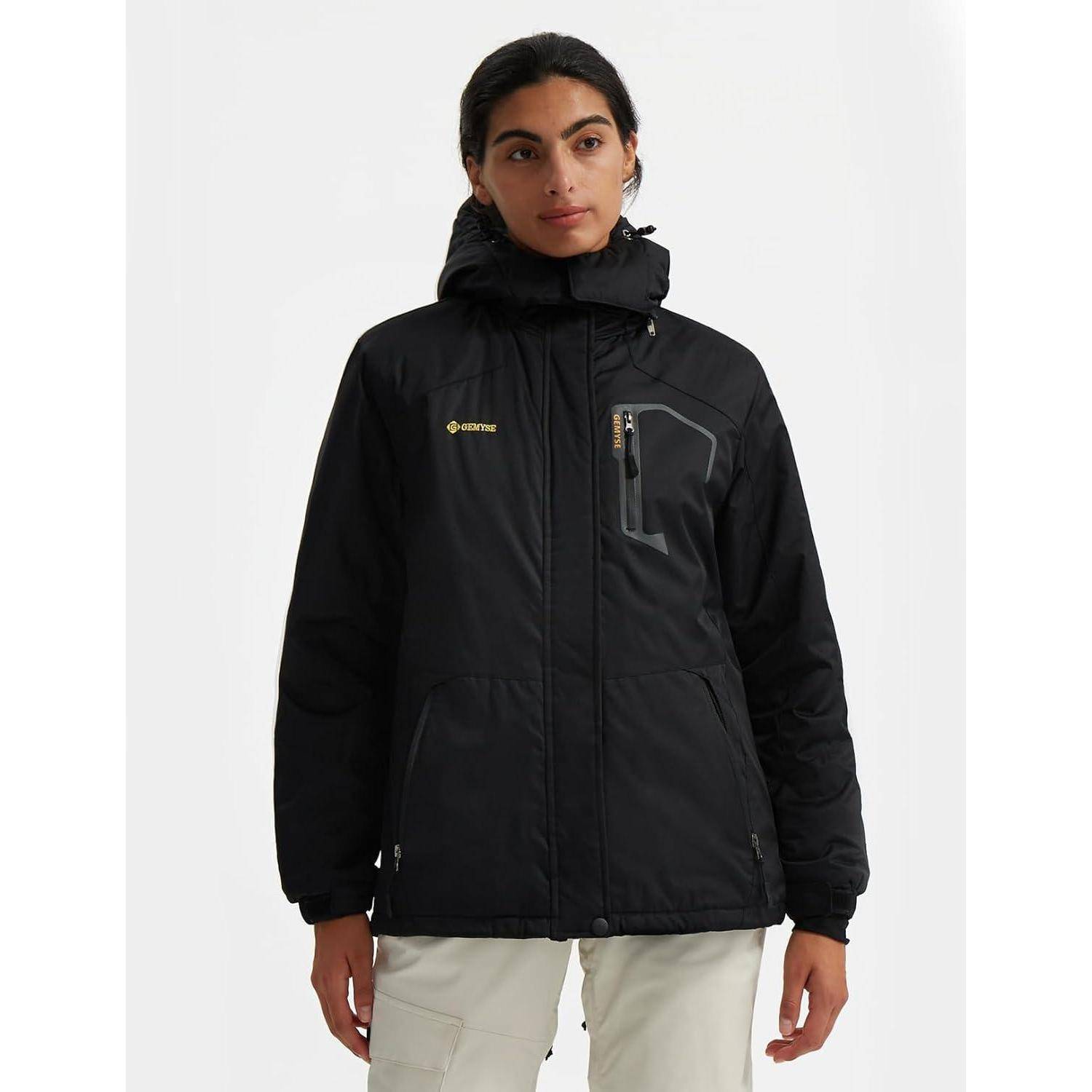 Eine Person, die eine schwarze Outdoor-Jacke mit hohem Kragen und Reißverschlusstaschen trägt, vor einem einfarbigen Hintergrund steht.