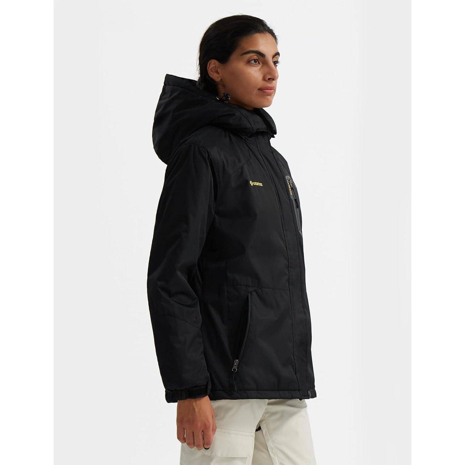 Eine Person trägt eine schwarze isolierte Jacke mit Kapuze und steht vor einem einfarbigen Hintergrund, seitlich blickend.