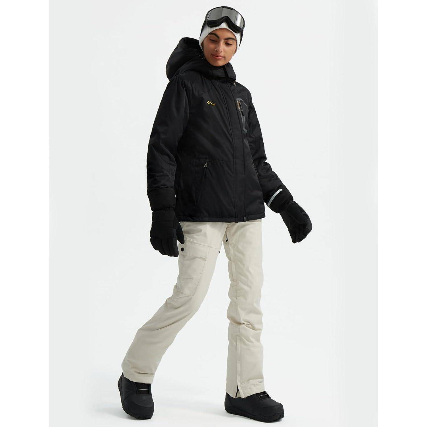 Eine Person in Winterkleidung steht auf Schnee und trägt eine schwarze Jacke, weiße Hose, Handschuhe und Stiefel, mit Skibrille auf dem Kopf.
