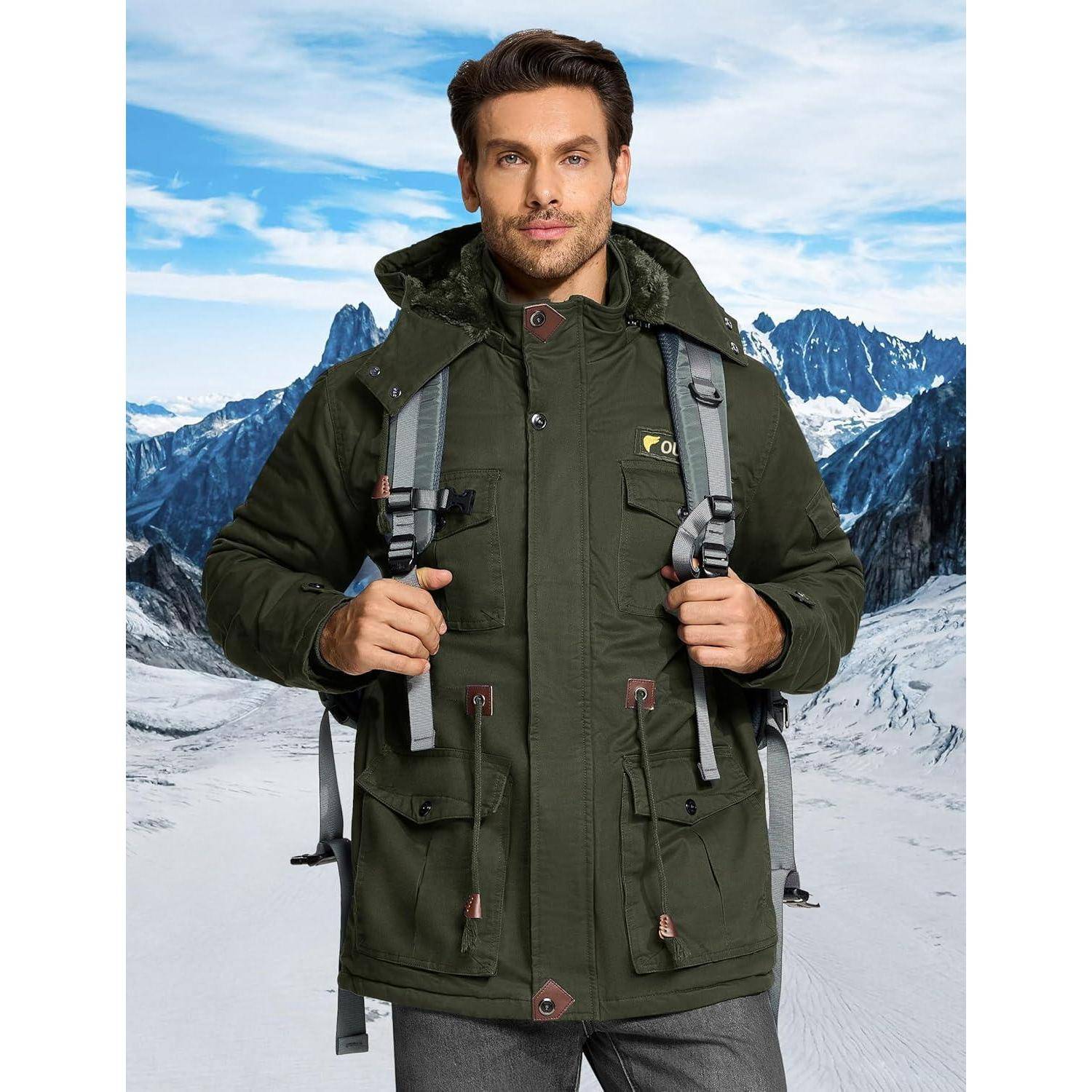 Eine Person mit einer grünen Jacke und einem Rucksack steht selbstbewusst auf einem schneebedeckten Bergpfad mit zerklüfteten Gipfeln im Hintergrund.