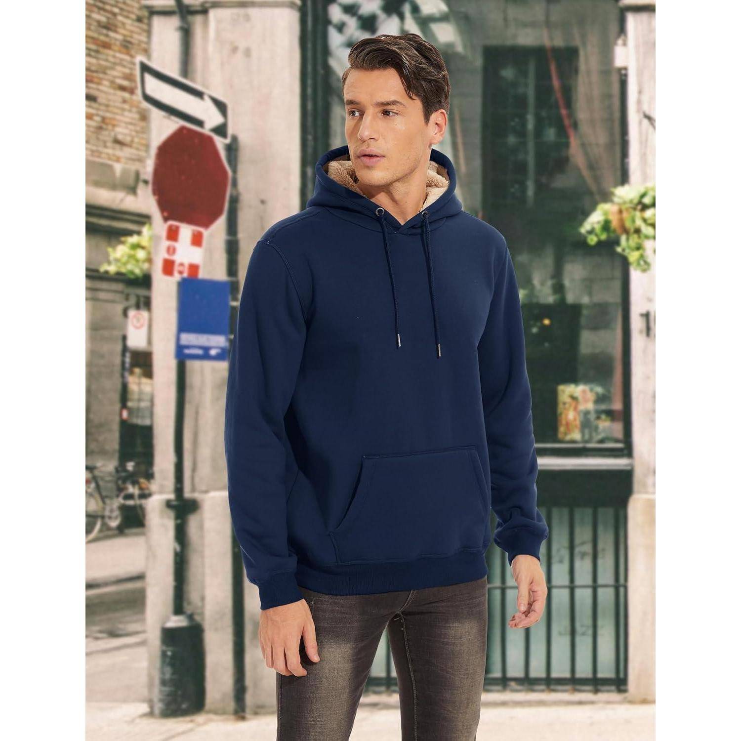 Eine Person trägt einen marineblauen Hoodie und Jeans und steht auf einer Stadtstraße. Ein Stoppschild und ein Gebäude sind im Hintergrund zu sehen.