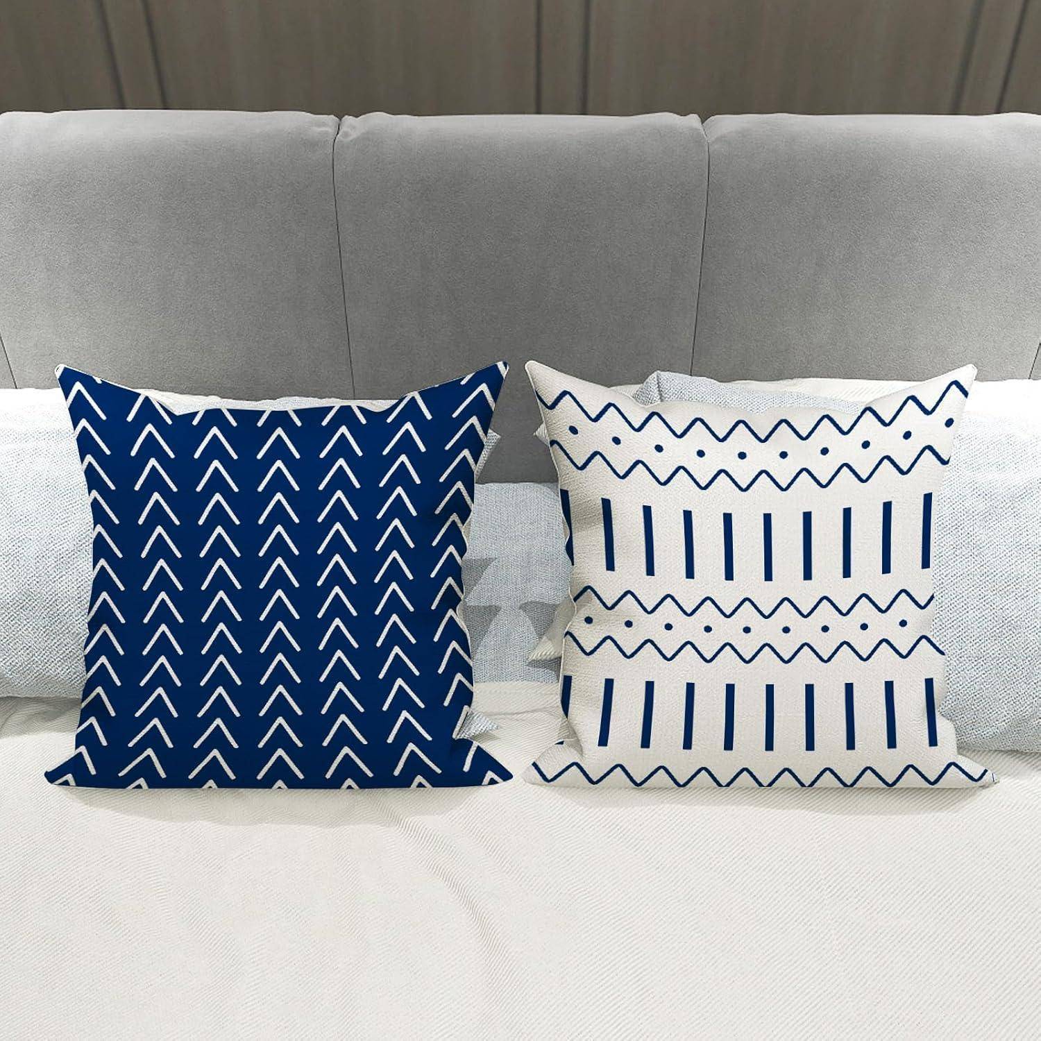 Zwei dekorative Kissen auf einem grauen Sofa: eines in Navy-Blau mit weißen Zickzack-Streifen, das andere weiß mit navy-blauen vertikalen Linien und Zickzack-Mustern.