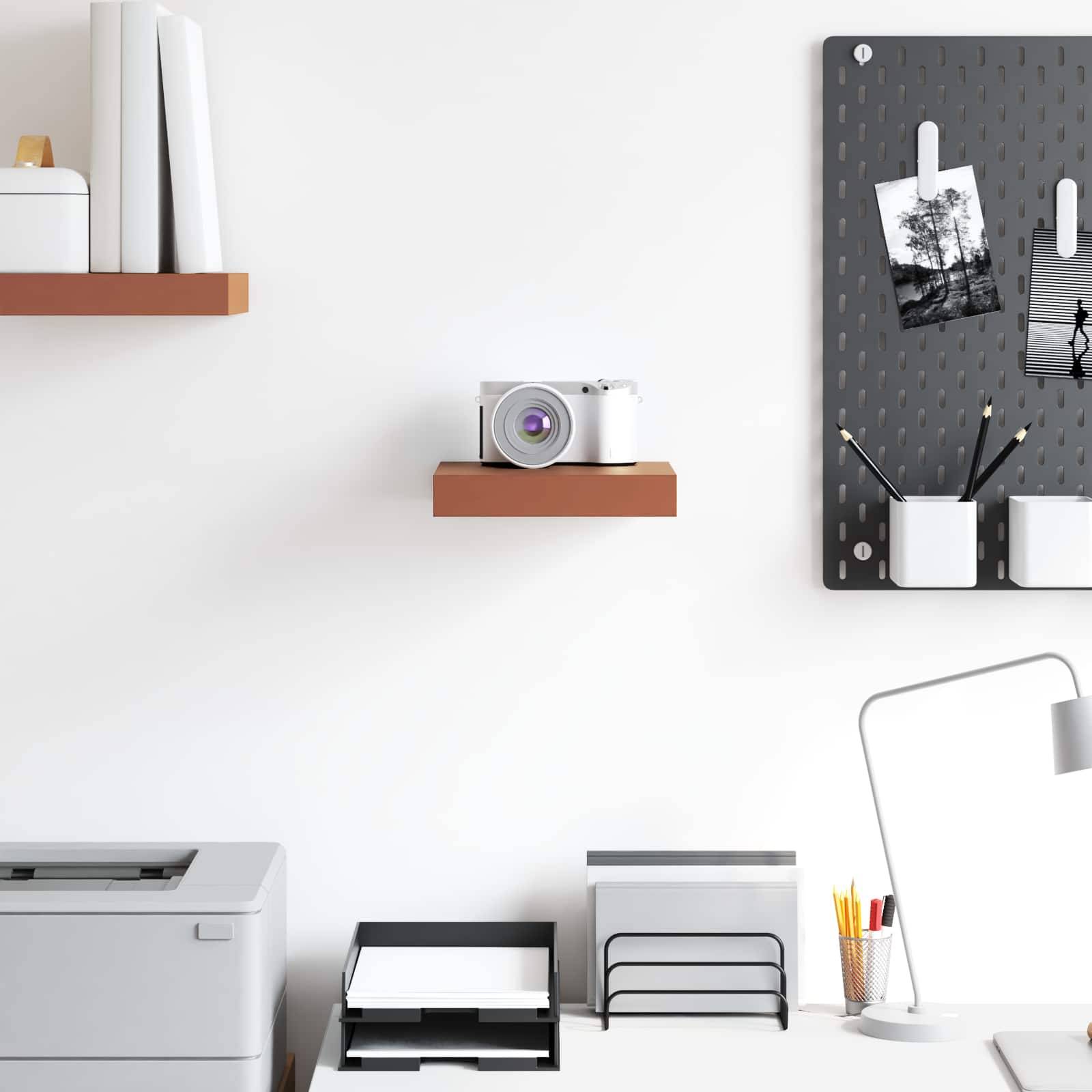 Ein modernes Büroschreibtisch-Setup mit Regalen, einem Drucker, einer Kamera und ordentlich organisiertem Schreibmaterial. Eine Lochplatte an der Wand hält Notizen und Fotos.