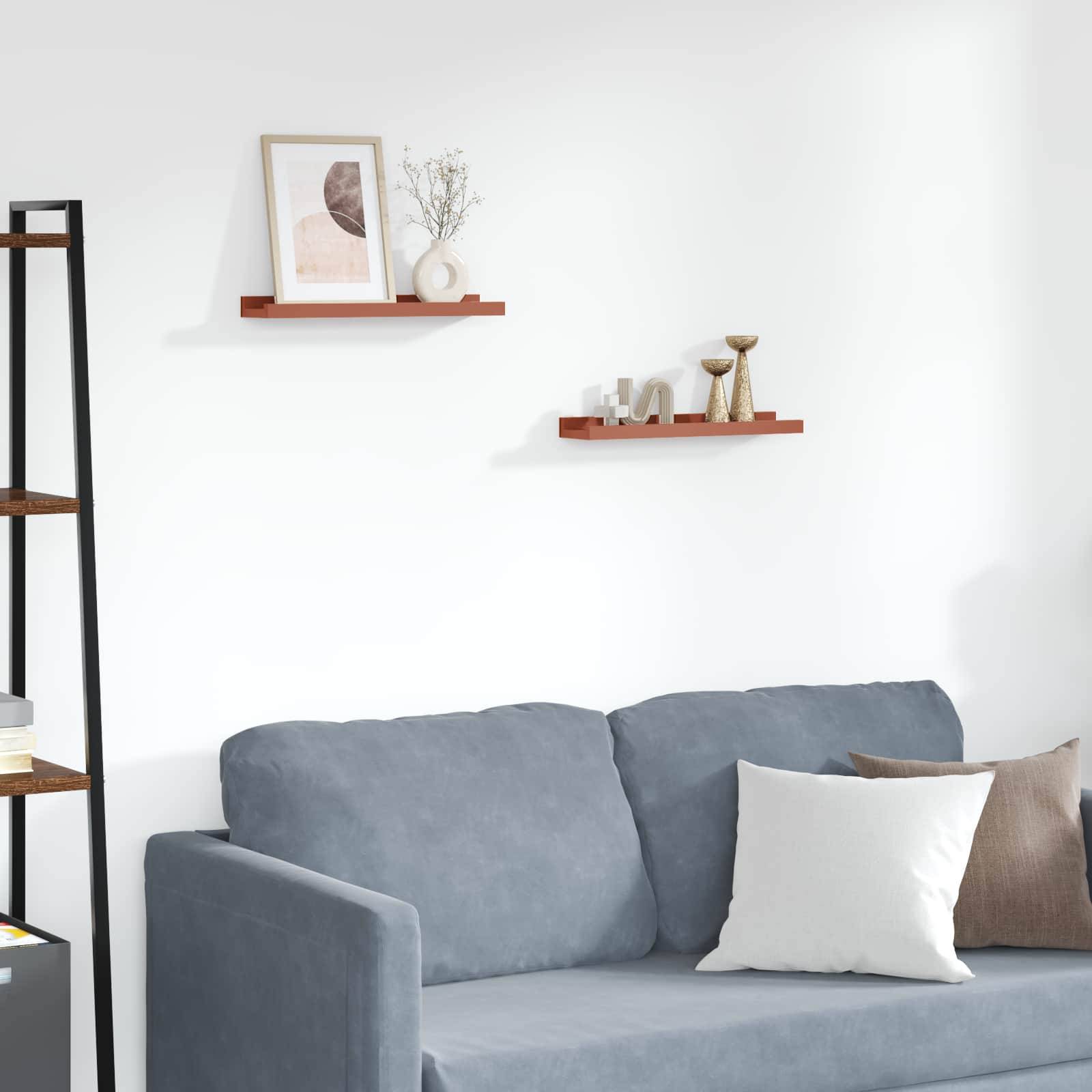 Eine gemütliche Ecke eines Wohnzimmers mit einem grauen Sofa und weißen Kissen. Zwei Holzregale schmücken die weiße Wand darüber und tragen Dekorationsgegenstände.