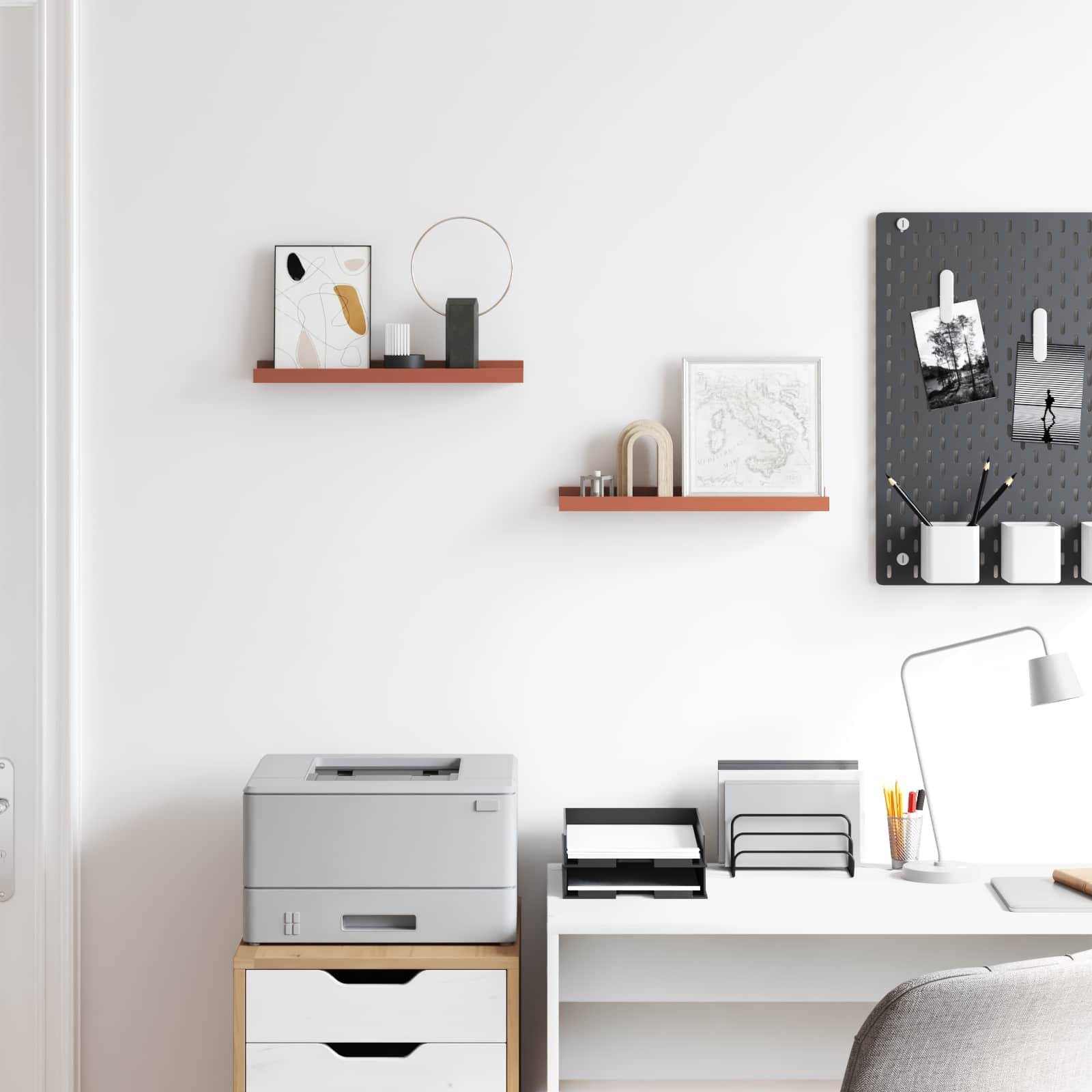 Eine minimalistische Ecke eines Home Office mit einem Drucker, organisierten Regalen und einer Whiteboard-Tafel mit Fotos, die eine aufgeräumte Arbeitsatmosphäre vermittelt.