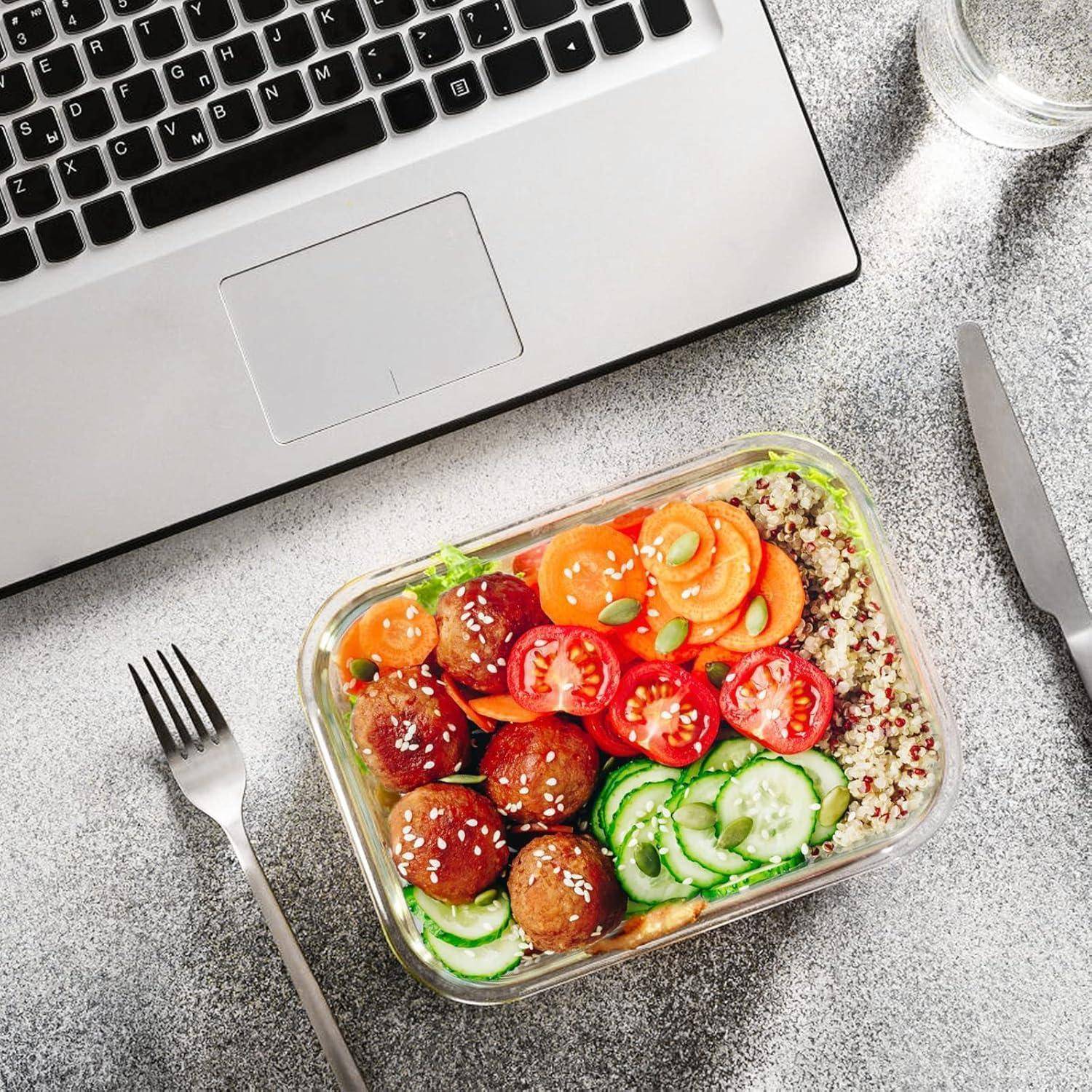 Ein Laptop und eine Gabel neben einem Behälter mit Quinoa, Salat, in Scheiben geschnittenen Gurken, Tomaten, Karotten und Falafel-Bällchen auf einer grauen Oberfläche.