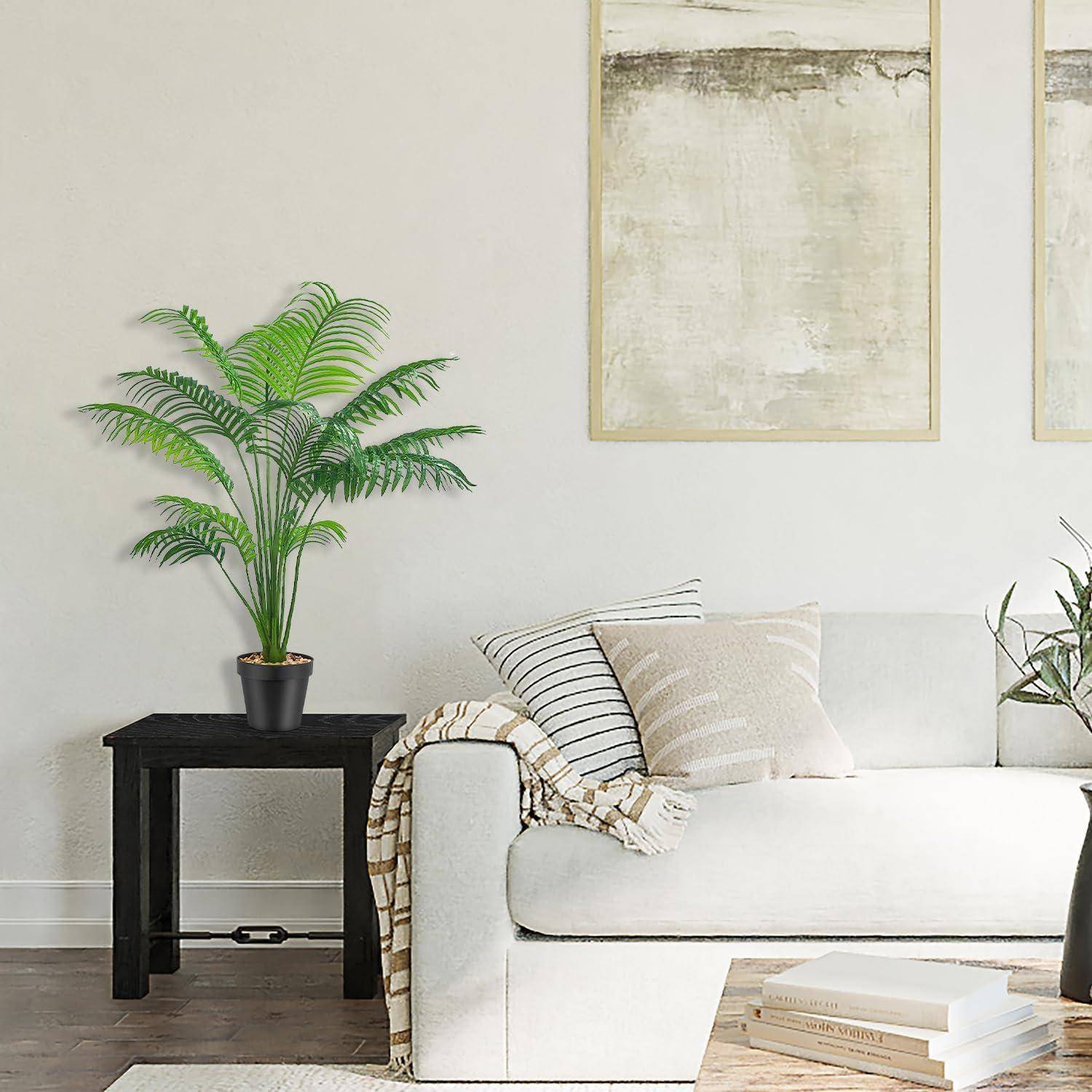 Ein gemütliches Wohnzimmer mit einem weißen Sofa, neutralen Kissen, einem schwarzen Beistelltisch mit einer Topfpflanze und zwei abstrakten Gemälden an der Wand.