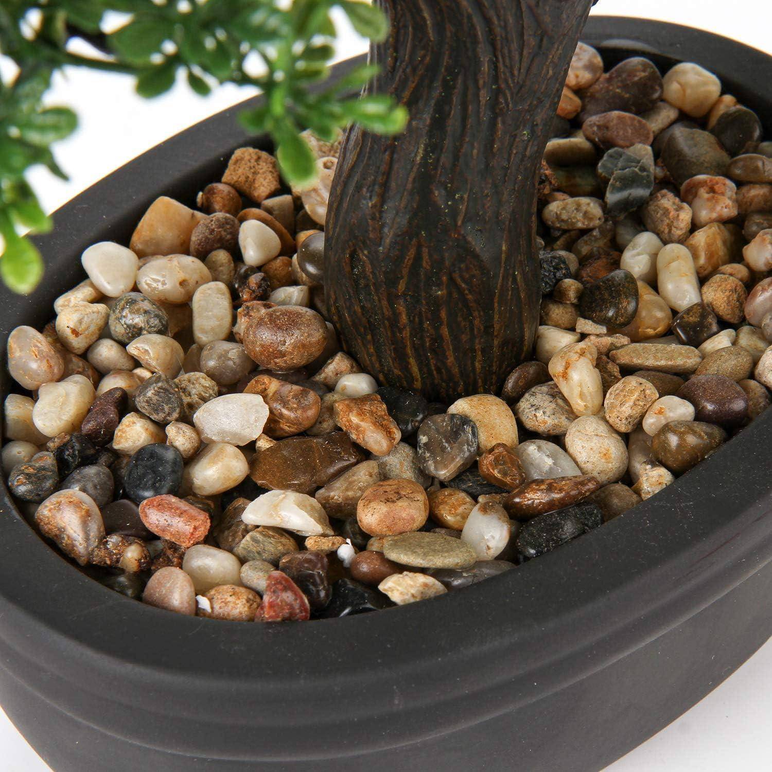 Ein kleiner künstlicher Baum mit realistischen grünen Blättern ist in einem schwarzen ovalen Topf gepflanzt, der mit einer Auswahl bunter Kieselsteine gefüllt ist.