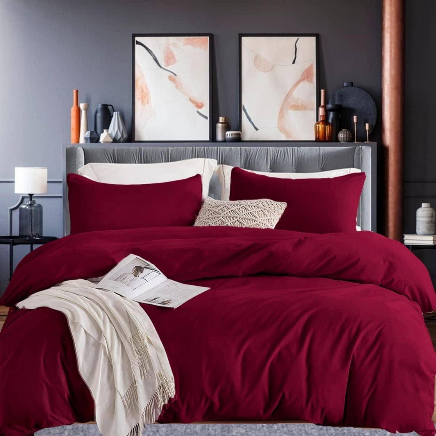 Ein ordentlich gemachtes Bett mit rot-weißer Bettwäsche, einem dekorativen Kissen und einer Decke. Zwei gerahmte abstrakte Kunstwerke hängen über dem Kopfteil.