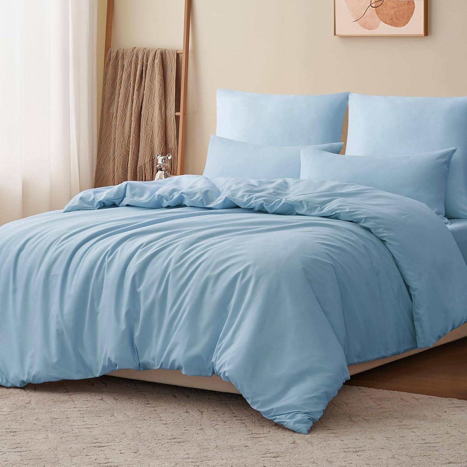 Ein ordentlich gemachtes Bett mit hellblauer Bettwäsche, vier Kissen und einer weichen grauen Decke, die über eine Ecke gebreitet ist; minimalistische, gemütliche Schlafzimmerdekoration.