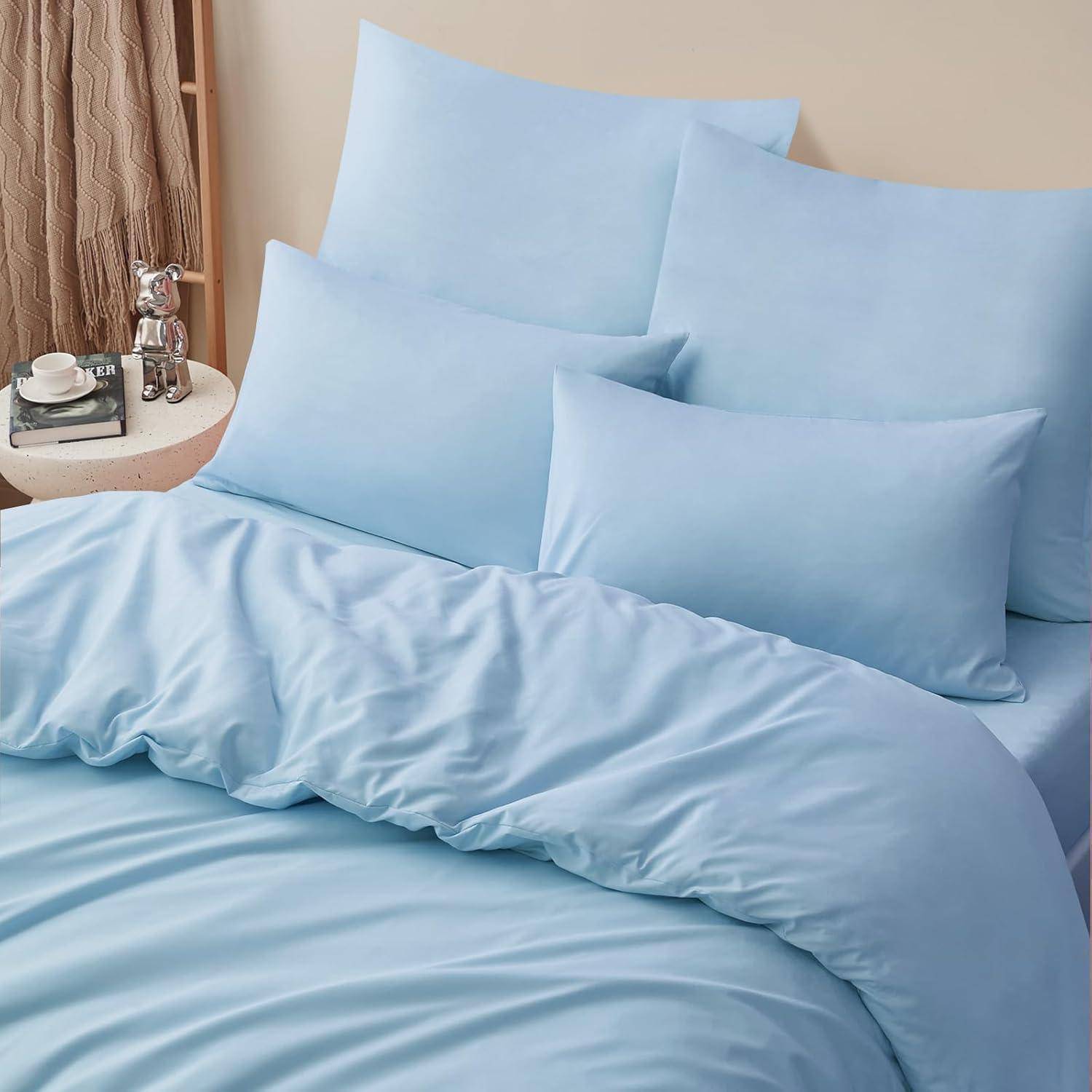 Ein ordentlich gemachtes Bett mit hellblauen Betttüchern und Kissen neben einem kleinen Tisch, auf dem eine silberne Hundestatue, eine Tasse und Bücher stehen.