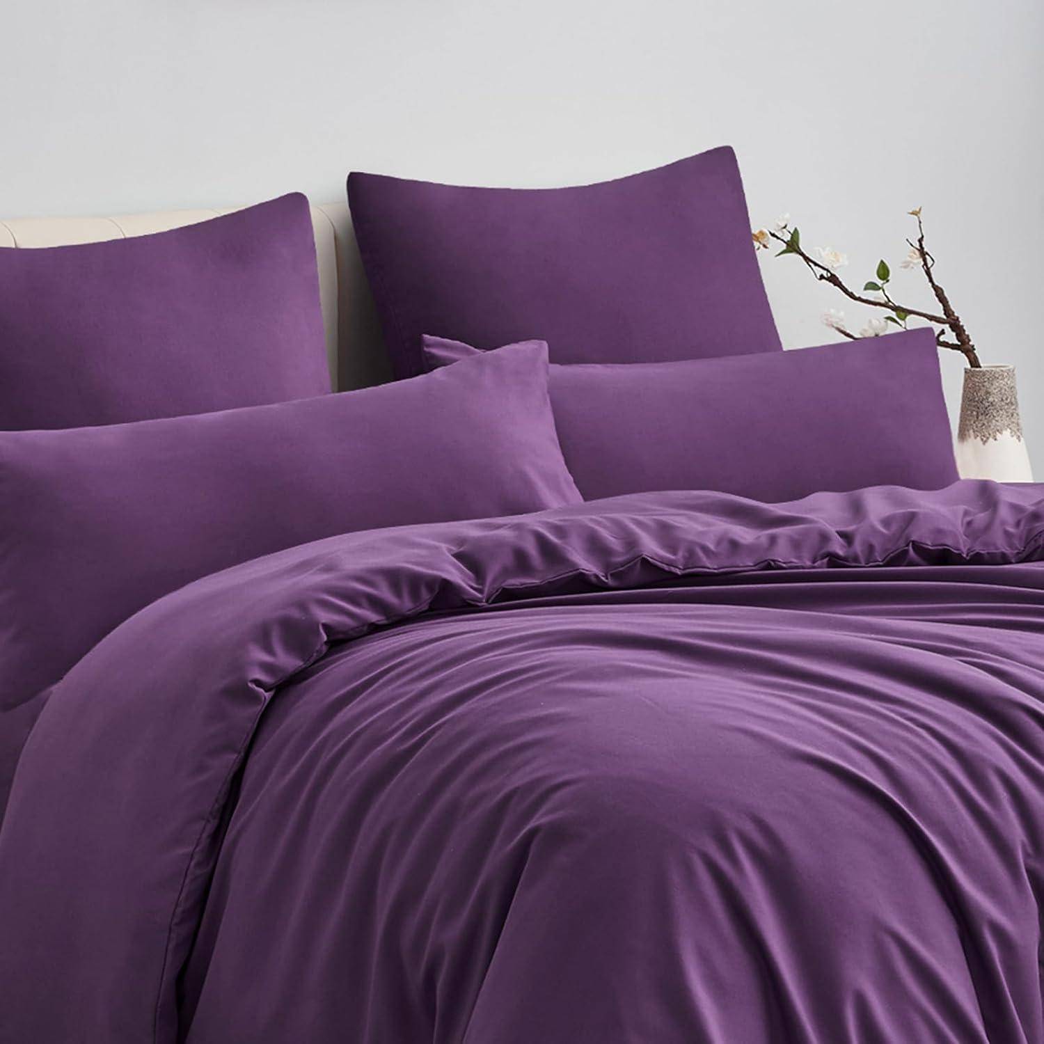 Lila Bettwäsche-Set bestehend aus Laken, Kissenbezügen und einer Bettdecke auf einem Bett, mit einer Vase mit einem Zweig auf dem Nachttisch.