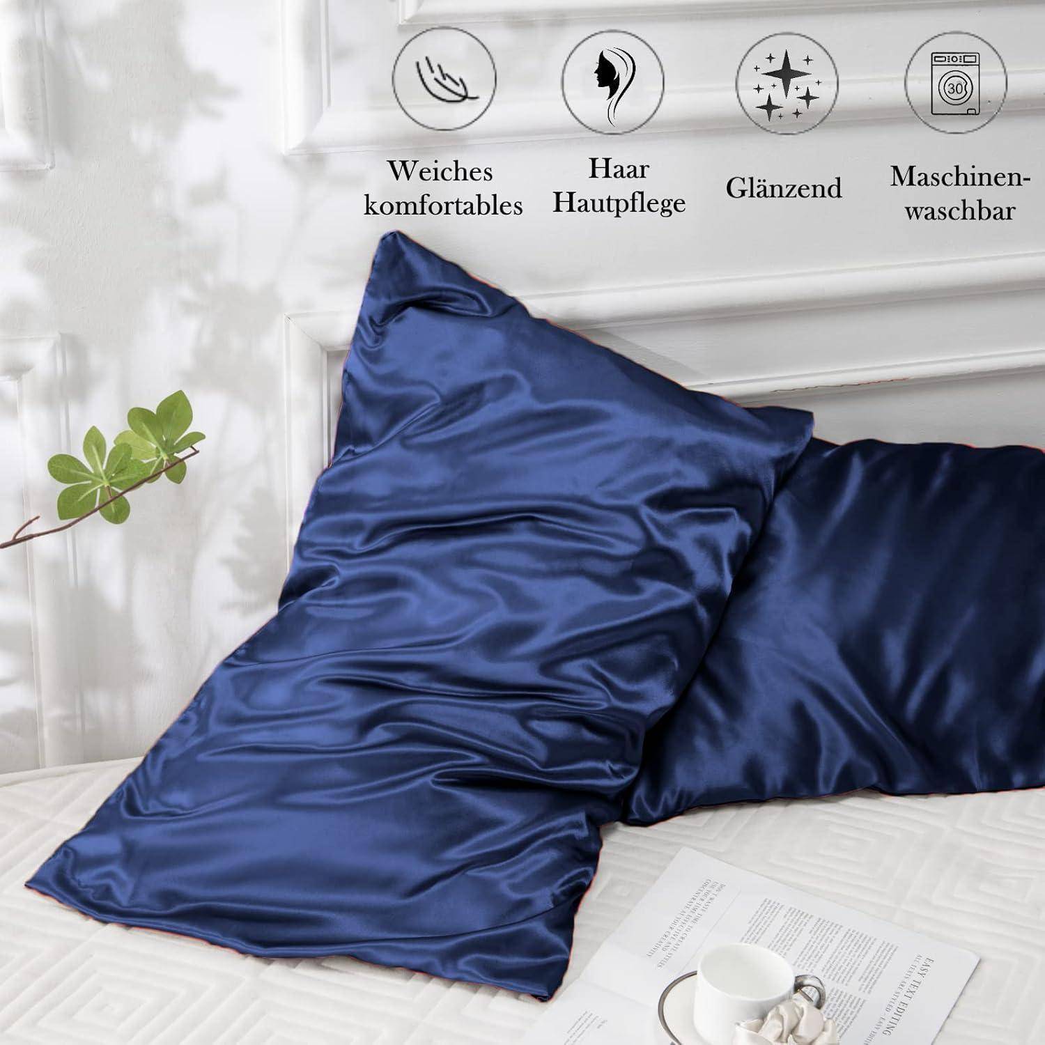 Ein Paar dunkelblaue Satin-Kissenbezüge auf einem weißen Bett, mit Symbolen, die Komfort, Haar- und Hautpflege sowie Maschinenwäsche anzeigen.