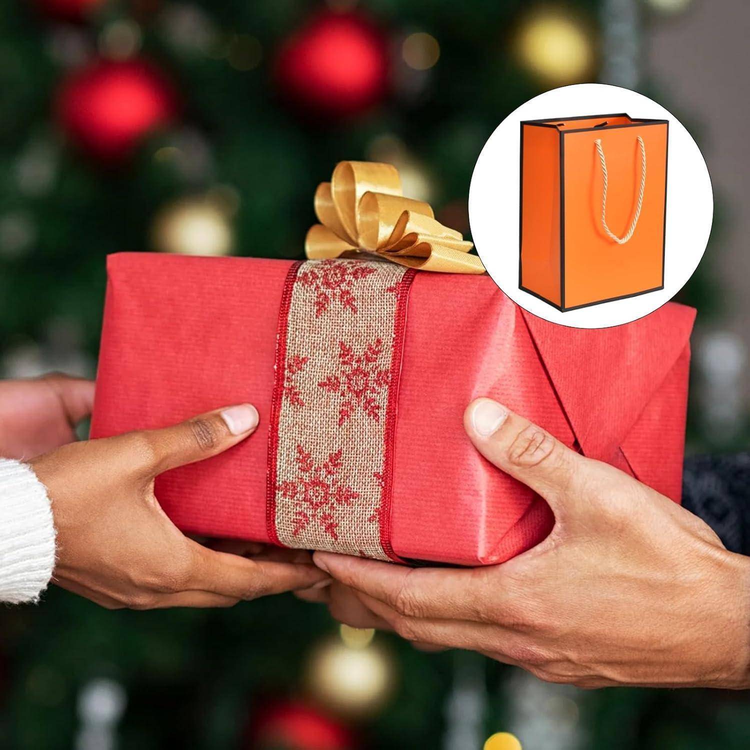Zwei Hände, die ein Geschenk mit einem roten Schneeflocken-Muster auspacken, vor einem festlichen, unscharfen Hintergrund. Ein orangefarbenes Einkaufstaschen-Icon ist eingebettet.