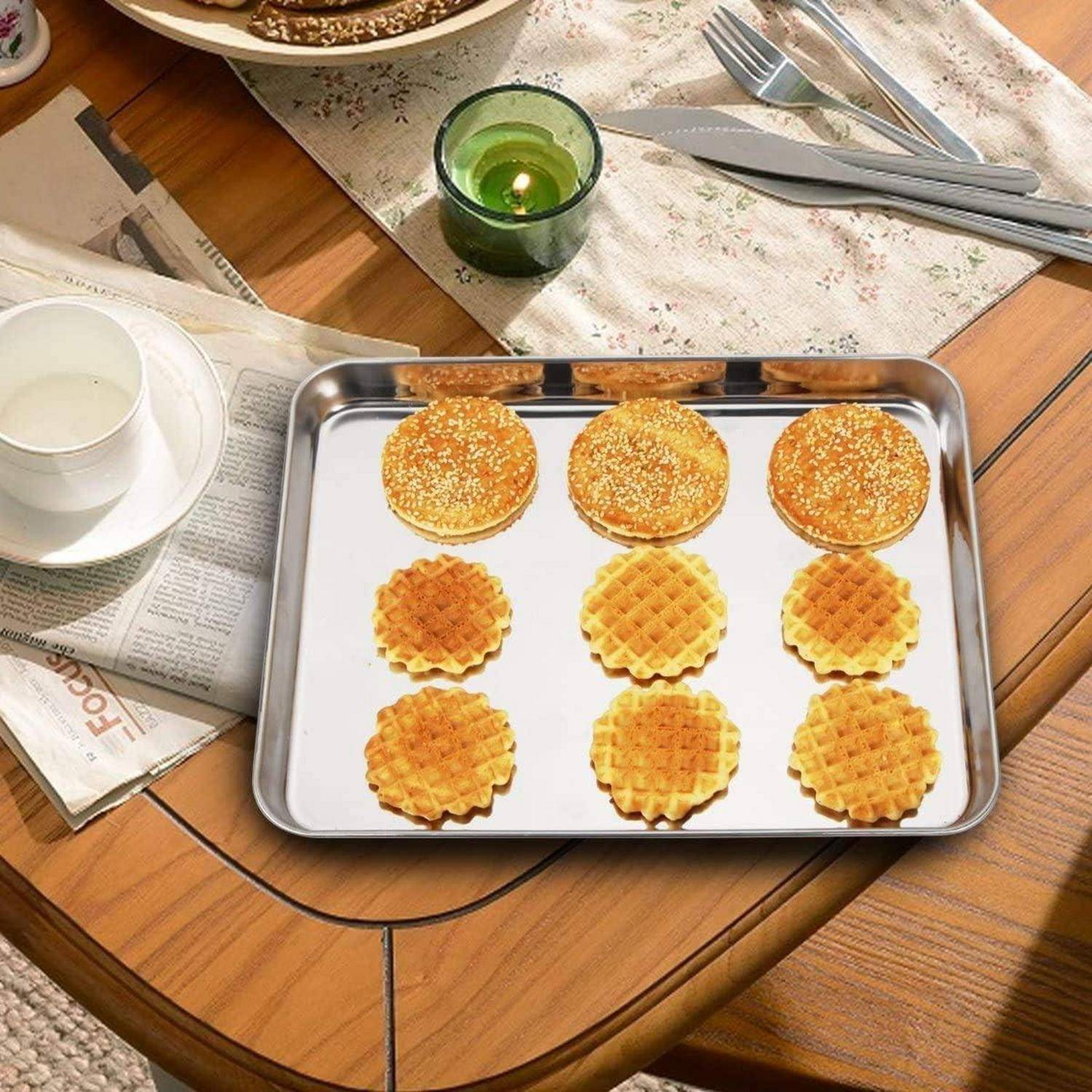 Ein Metalltablett auf einem Holztisch hält neun goldene, runde Waffeln. In der Nähe des Tabletts stehen ein Glas Milch, eine Kerze, Besteck und eine Zeitung.
