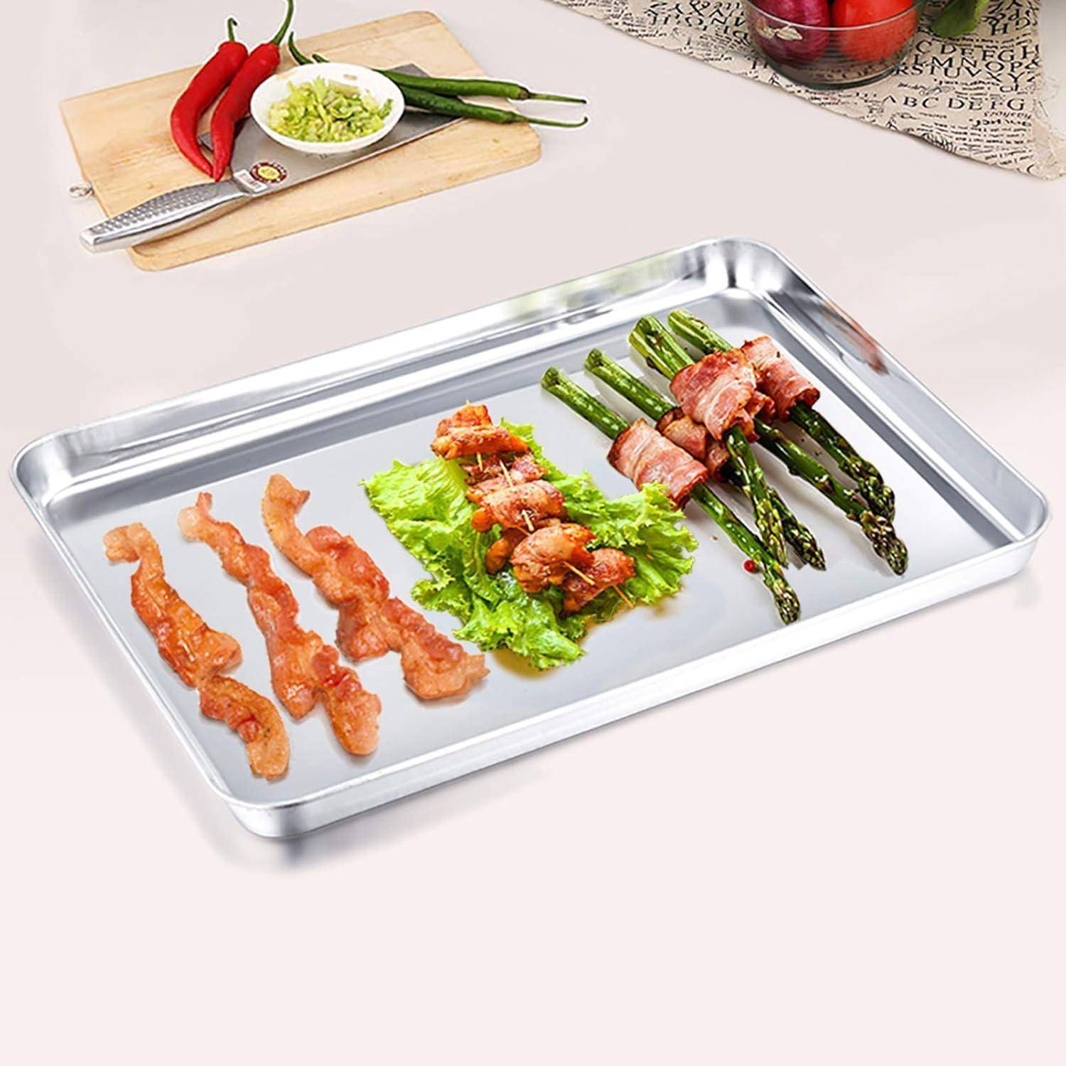 Ein Metalltablett mit gebratenem Bacon, Salat und in Bacon gewickeltem Spargel auf weißem Hintergrund. Gehackte Frühlingszwiebeln und rote Chilischoten auf einem Holzbrett im Hintergrund.
