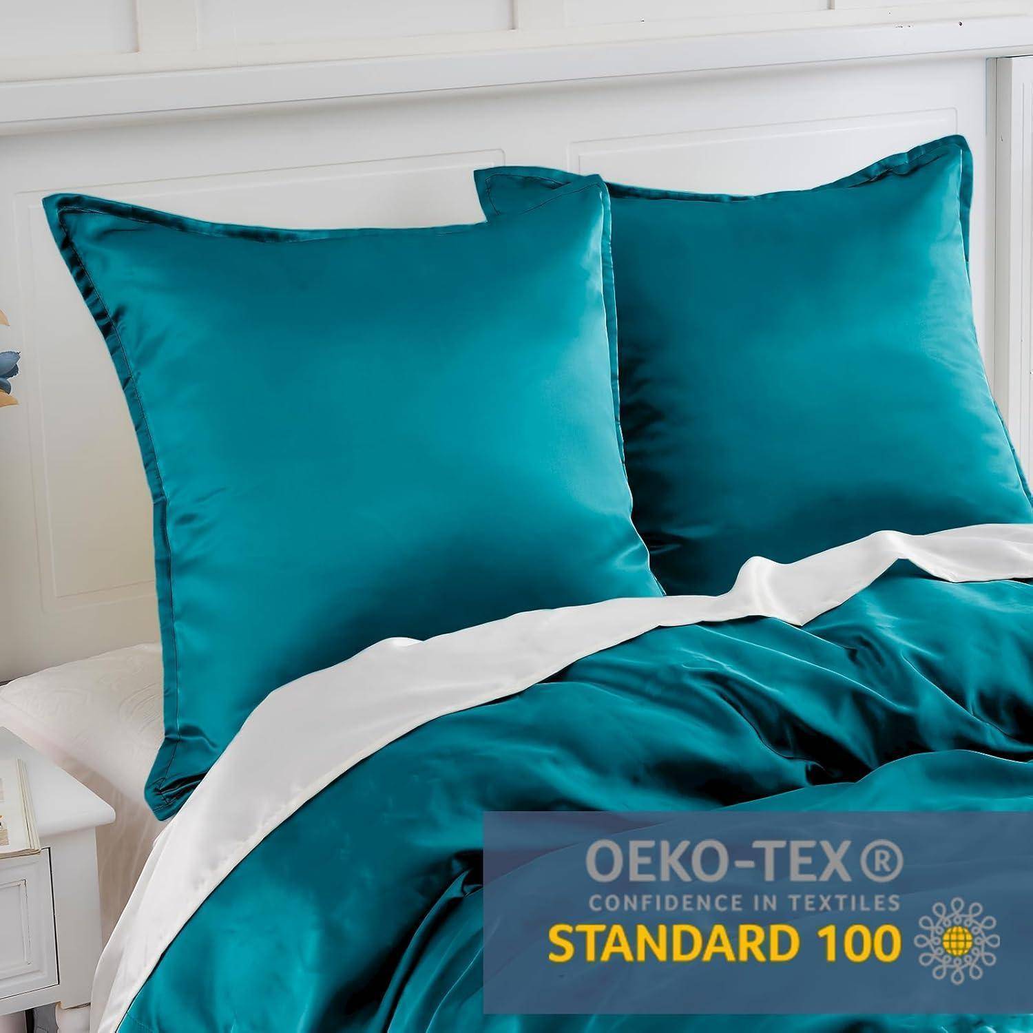 Zwei petrolblaue Kissen und eine passende Bettdecke auf einem Bett. Ein Etikett zeigt: 'OEKO-TEX Vertrauen in Textilien STANDARD 100'.