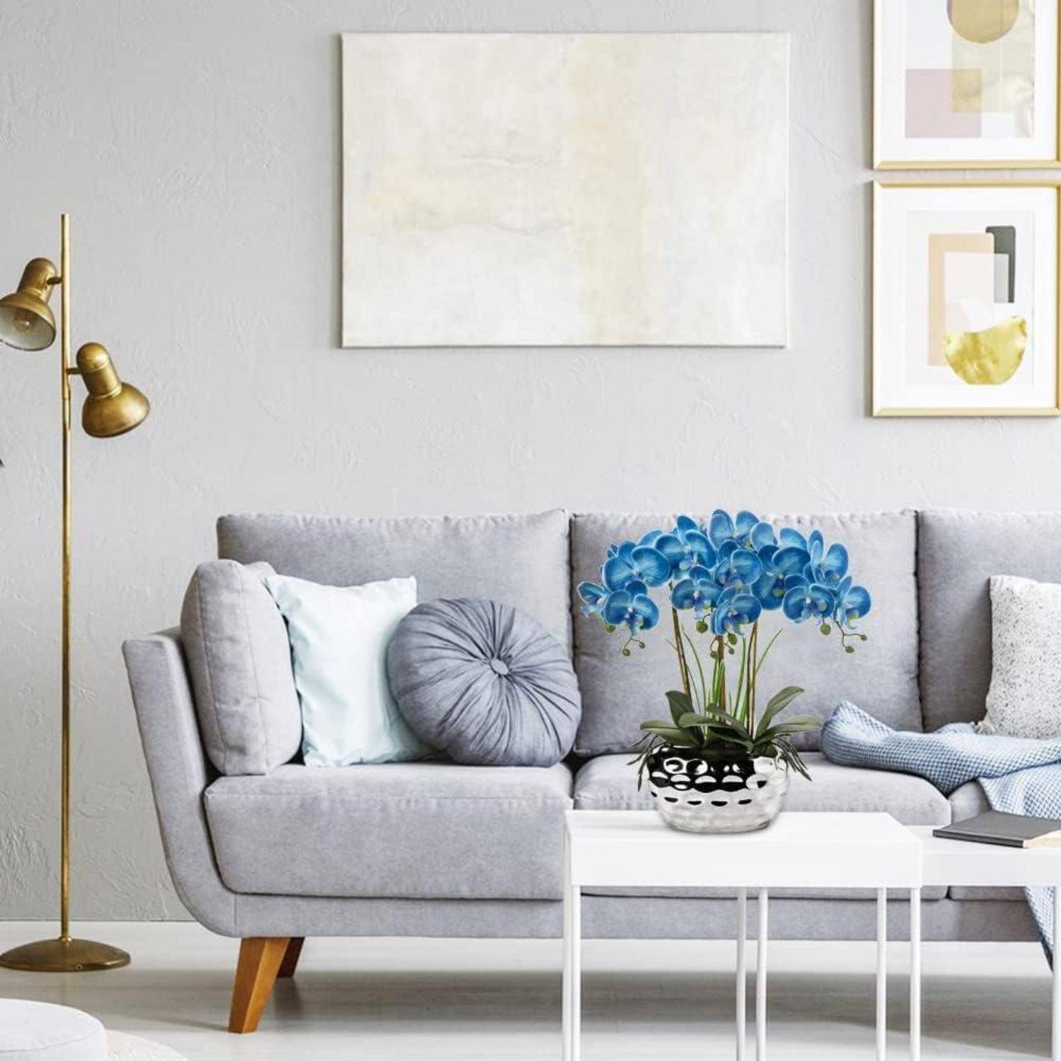 Ein modernes Wohnzimmer mit einem grauen Sofa, weißen und grauen Kissen, einer Glasvase mit blauen Blumen auf einem weißen Couchtisch und abstrakter Wandkunst.