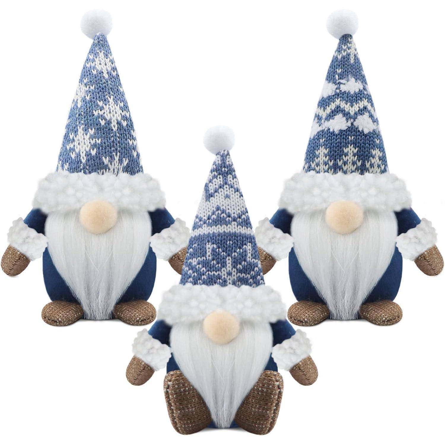 Drei Plüsch-Gnome mit blauen Strickmützen, weißen Bärten und braunen Schuhen stehen nebeneinander. Jeder trägt einen flauschigen weißen Besatz an der Mütze.