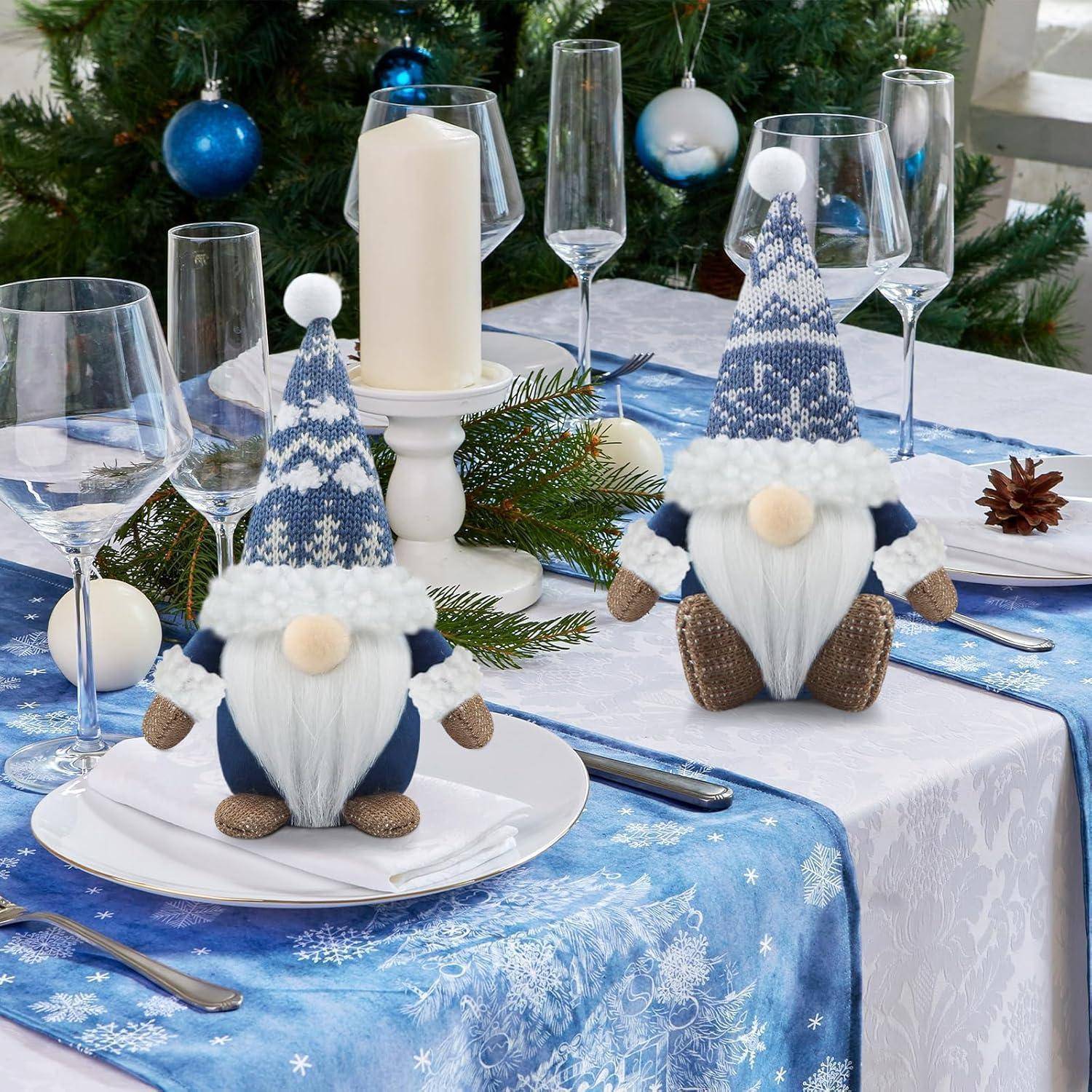 Festlich gedeckter Esstisch mit blau-weißem Thema, mit zwei Gnom-Figuren mit gestrickten Mützen, umgeben von Kerzen und Weihnachtsdekoration.