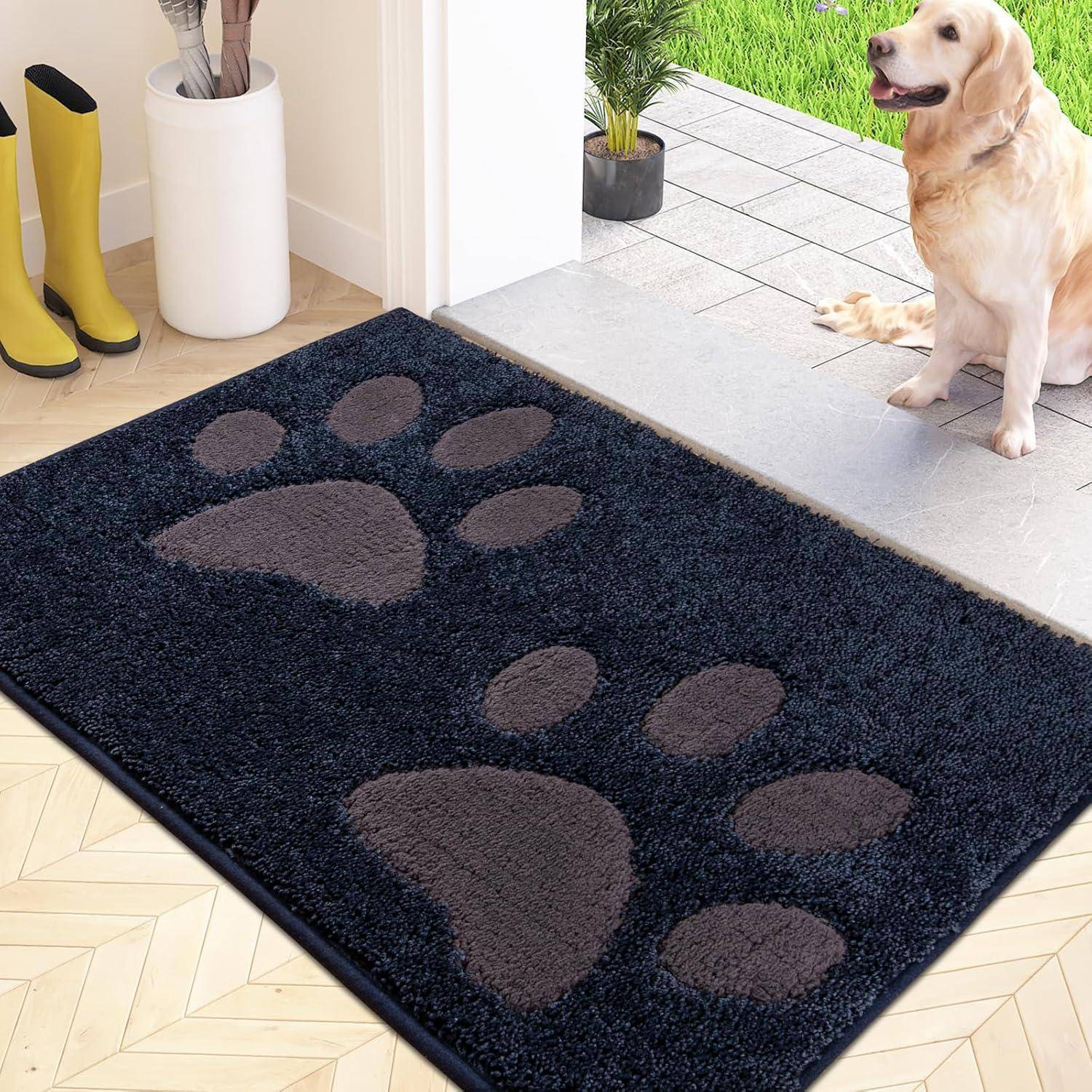 Eine große schwarze Fußmatte mit Pfotenabdruckmustern liegt auf einem gefliesten Boden, neben gelben Stiefeln und einem Hund, der neben dem Türeingang sitzt.