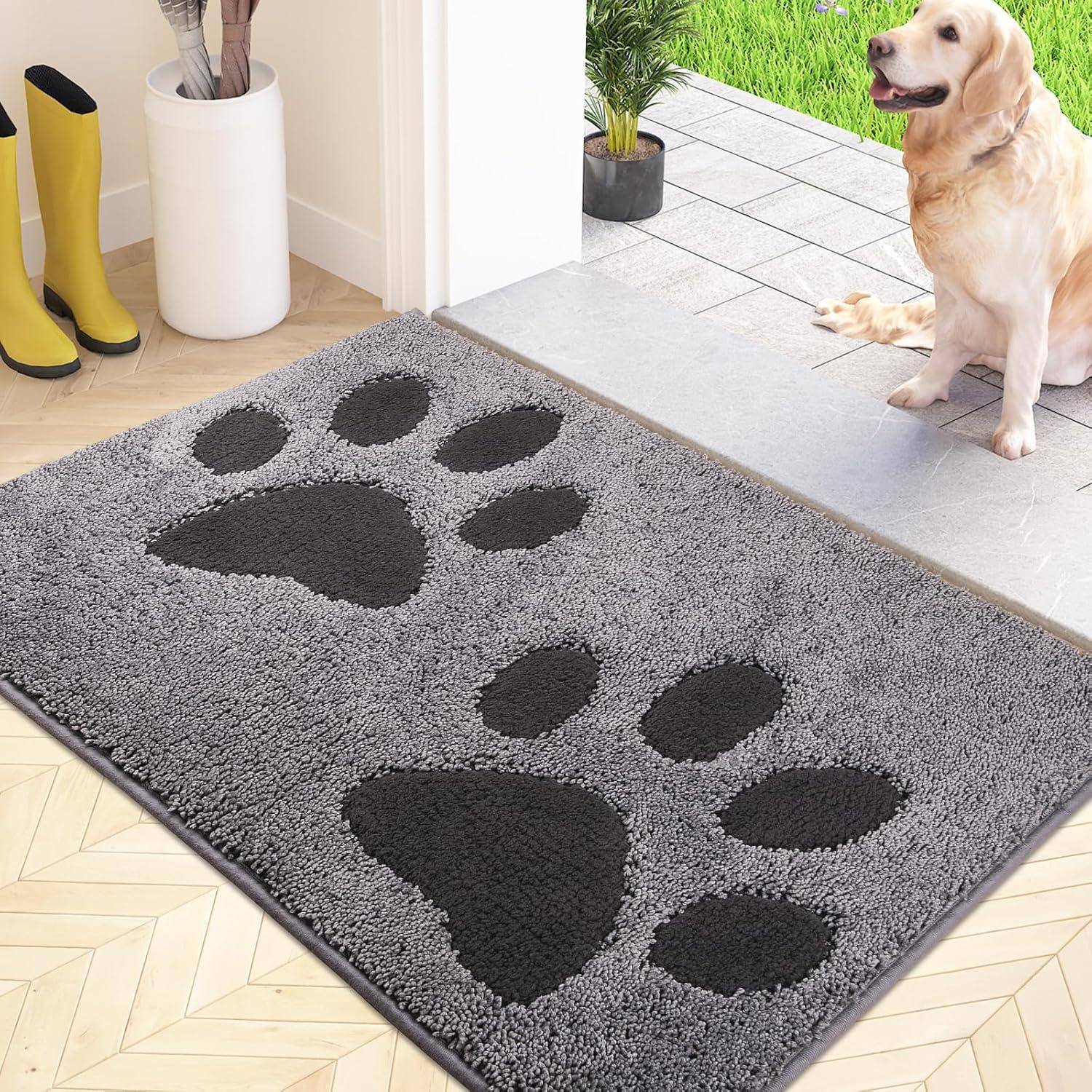 Eine graue Matte mit großen schwarzen Pfotenabdrücken, die auf einem Holzboden liegt, in der Nähe einer offenen Tür, die nach draußen führt, mit einem Hund, der daneben sitzt.