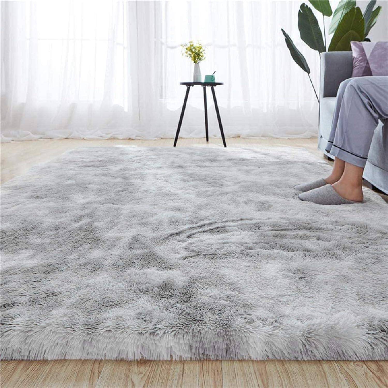 Ein flauschiger, grauer Teppich in einem Wohnzimmer mit einem runden Tisch, einer Topfpflanze und einem Teil eines Sofas, der eine gemütliche, moderne Atmosphäre schafft.