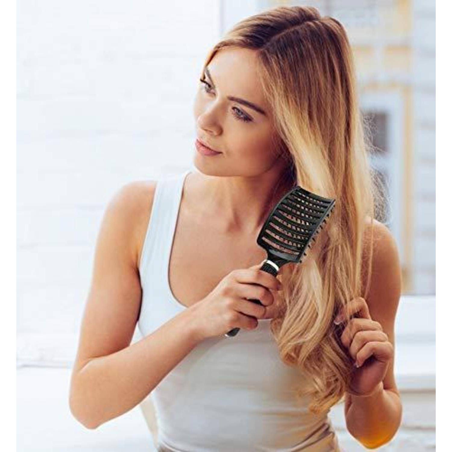 Eine Person mit langen, blonden Haaren bürstet ihre Haare mit einer schwarzen Bürste und steht in einer hellen Inneneinrichtung.
