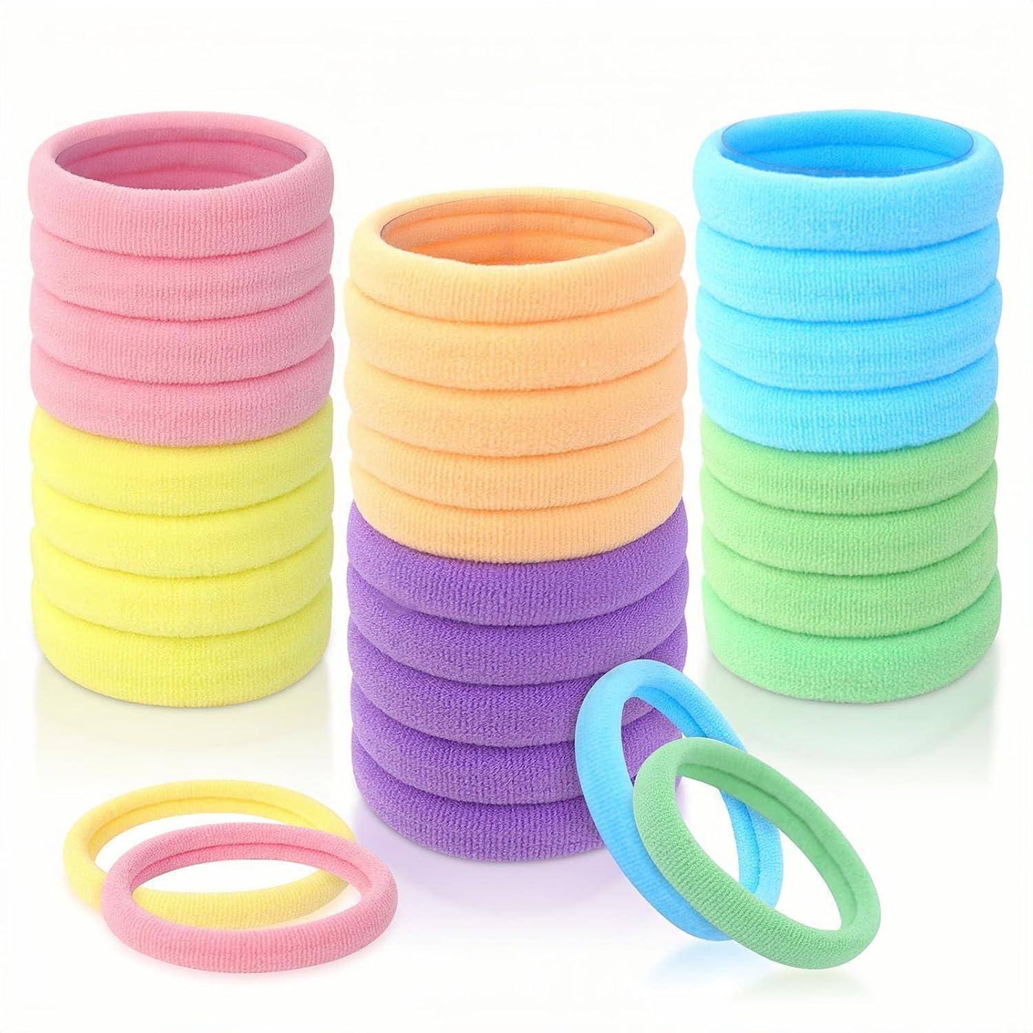 Bunte elastische Haargummis in Stapeln von rosa, orange, gelb, lila, blau und grün in Reihen angeordnet. Zwei zusätzliche Haargummis davor.