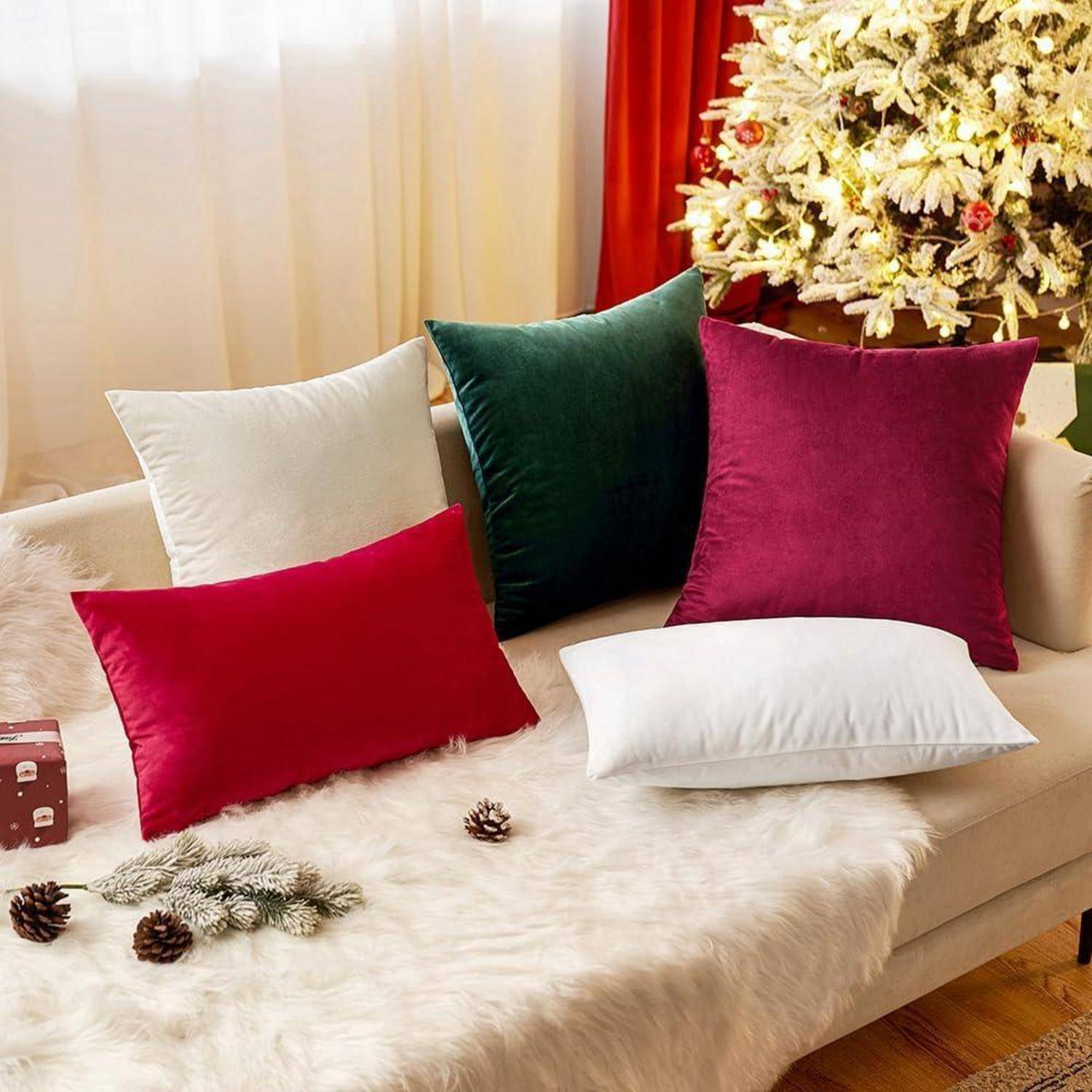 Eine gemütliche Szene mit einem weißen Fellüberwurf, roten und grünen Samtkissen und einem geschmückten Weihnachtsbaum im Hintergrund. Tannenzapfen verleihen eine natürliche Note.