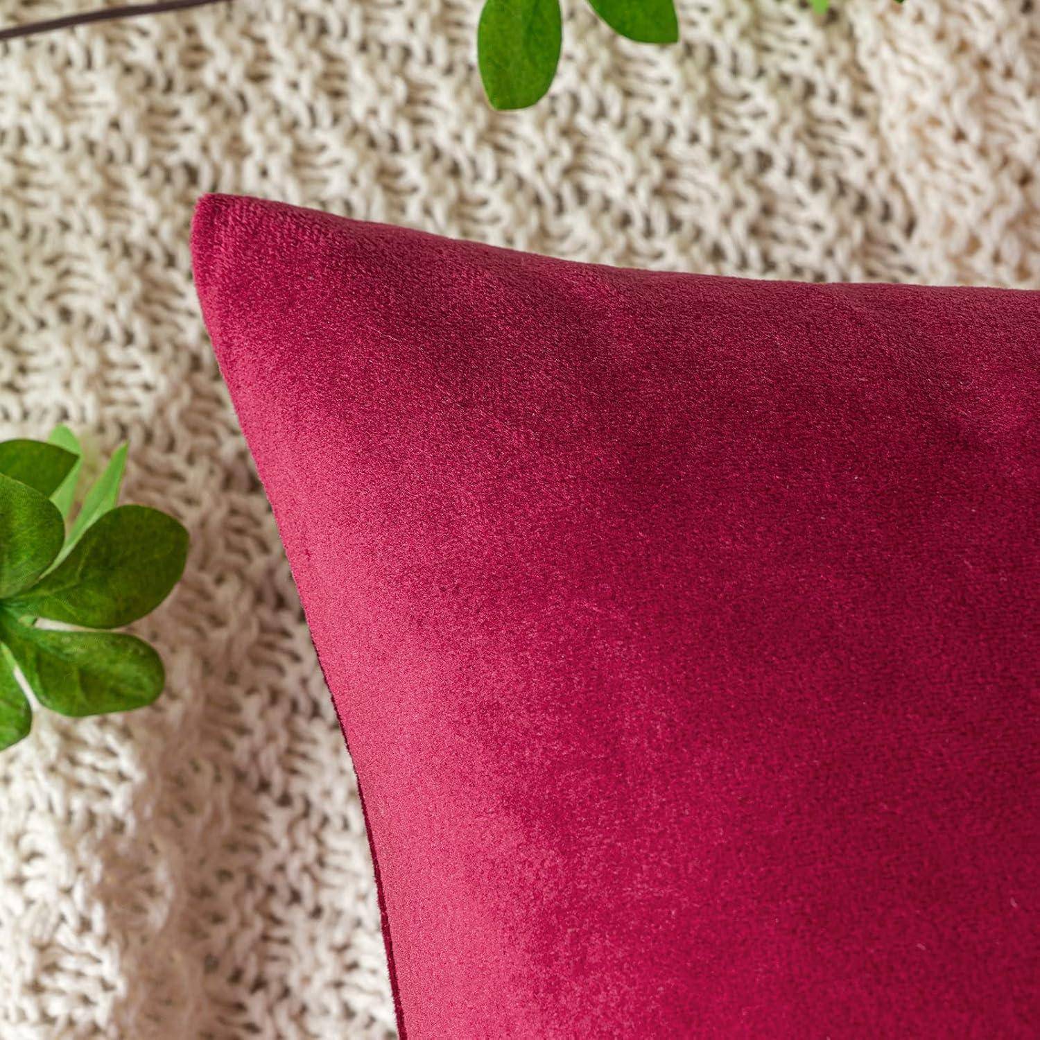 Ein roter Samtkissen auf einer gestrickten beigen Decke, mit grünen Pflanzenblättern in der Nähe.