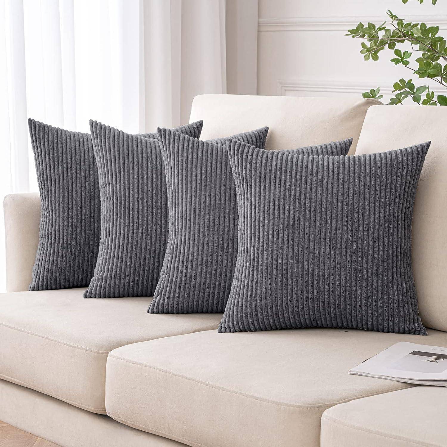 Ein beiges Sofa mit fünf grauen, gerippten Kissen in einer Reihe. Eine Zeitschrift liegt in der Nähe, und ein Teil einer Topfpflanze ist im Hintergrund zu sehen.