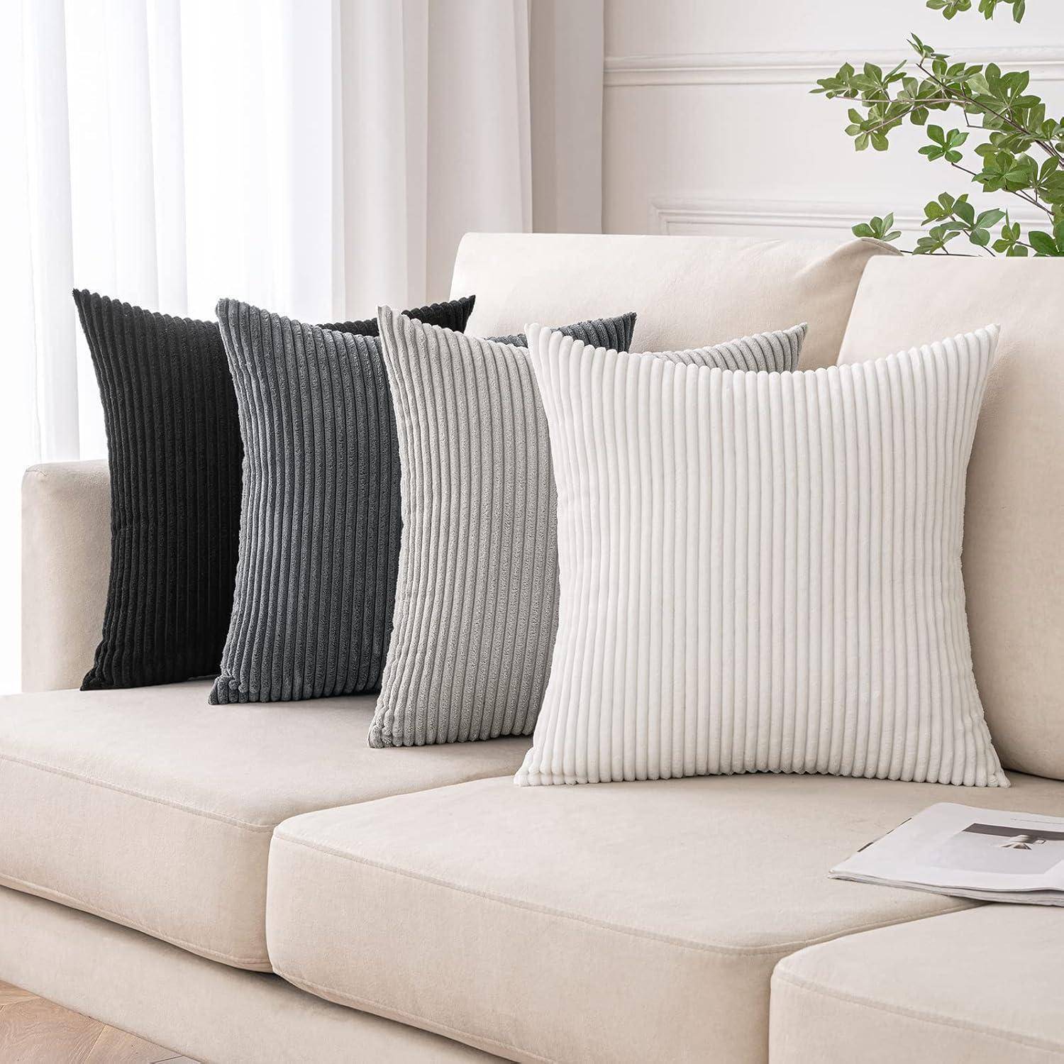 Vier gerippte Kissen in Grau- und Weißtönen sind ordentlich auf einem beigen Sofa angeordnet. Eine kleine Pflanze schmückt den Hintergrund.