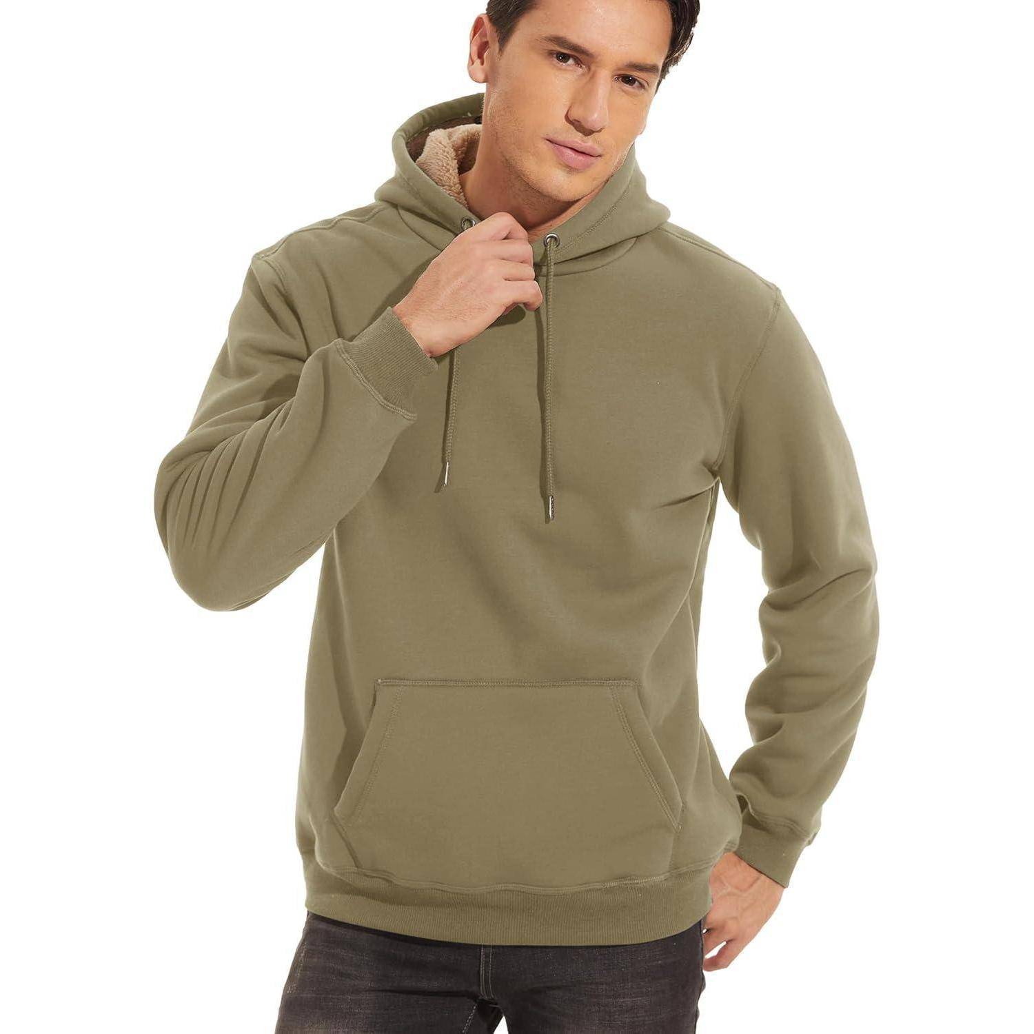 Eine Person, die einen grünen Hoodie trägt und mit einer Hand am Kapuzensaum posiert. Sie steht vor einem einfarbigen weißen Hintergrund.