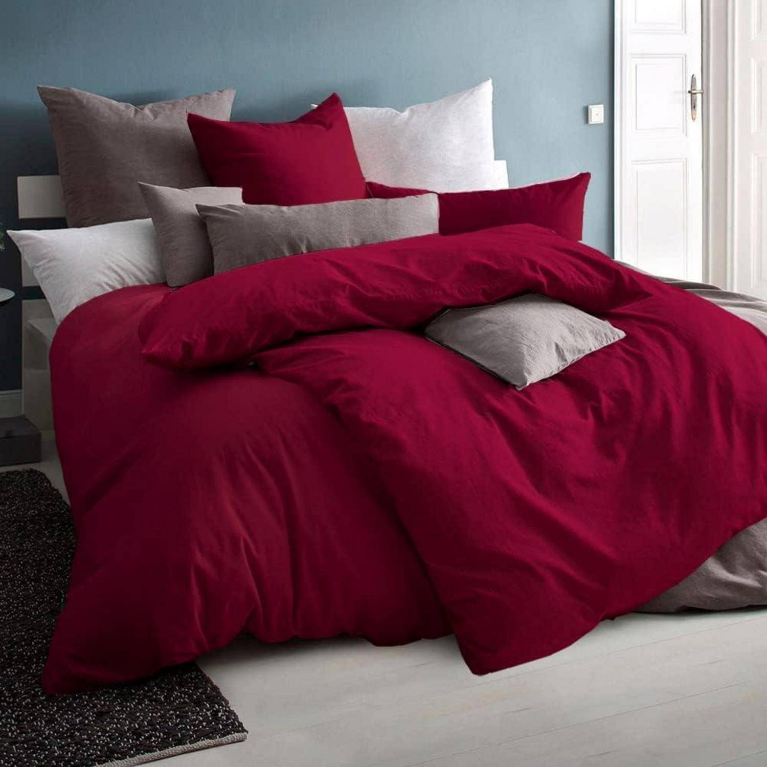Ein ordentlich gemachtes Bett mit roten und grauen Kissen und einer roten Bettdecke in einem Raum mit grauen Wänden.