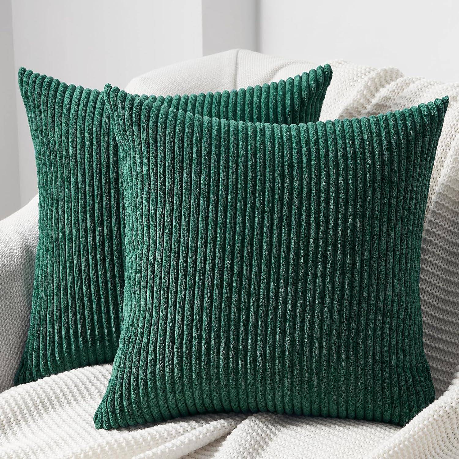 Zwei grüne, gerippte Kissen auf einer gestrickten cremefarbenen Decke auf einem hellgefärbten Sofa, die einen gemütlichen und stilvollen Wohnbereich schaffen.