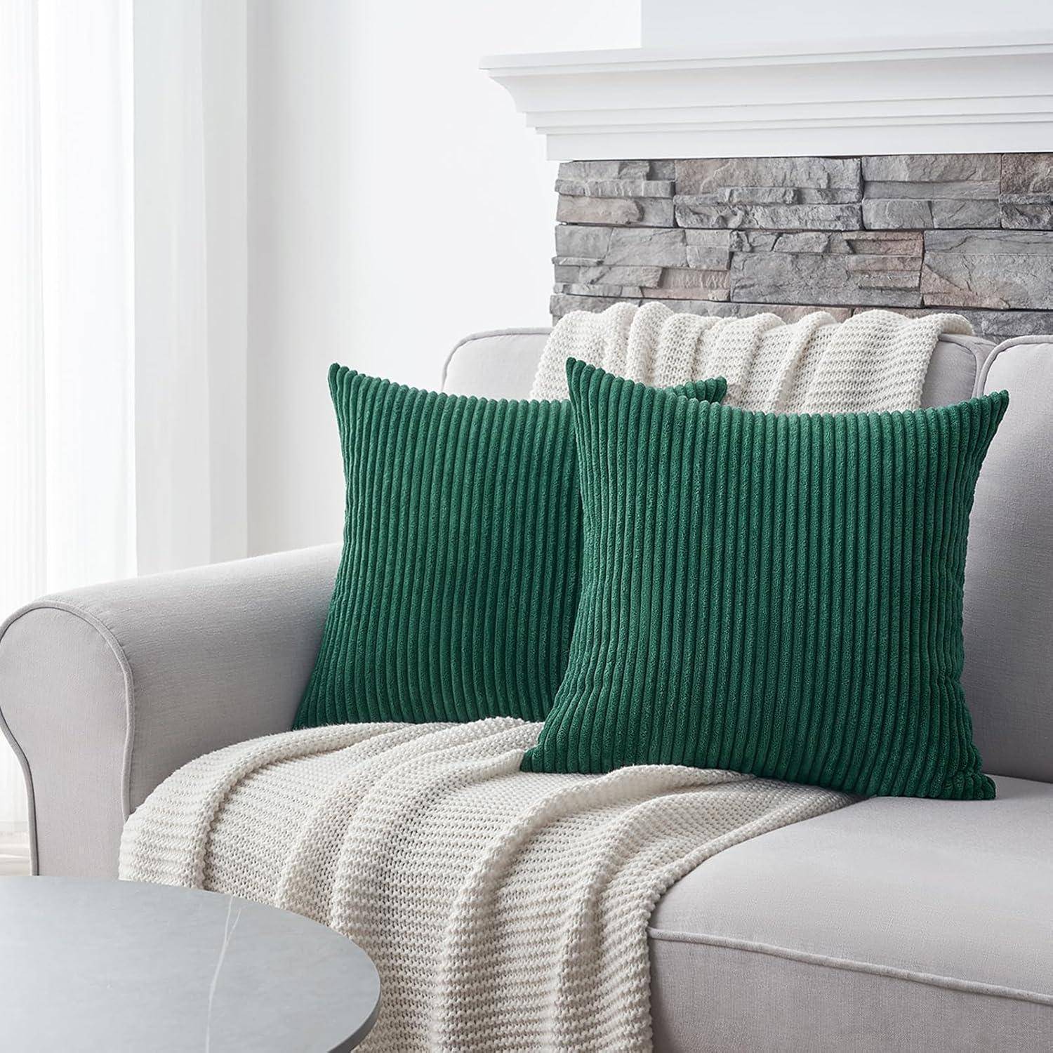Ein grauer Sofa mit einer hellen gestrickten Decke und zwei grünen Corduroy-Kissen steht vor einem Steinkatmin.