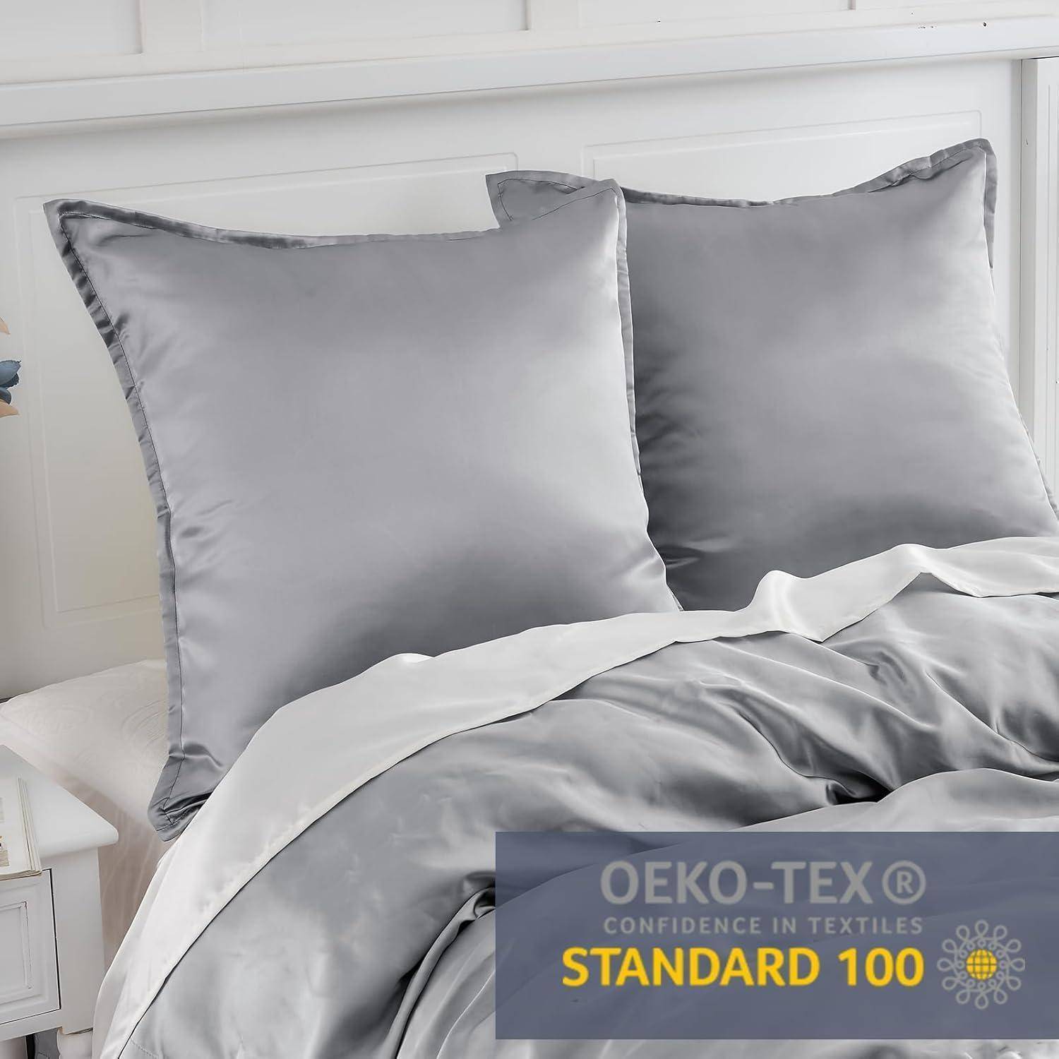 Zwei silbergraue Kissen und eine passende Bettdeckenhülle auf einem Bett, mit einem 'OEKO-TEX STANDARD 100' Etikett, das die Textilsicherheit gewährleistet.