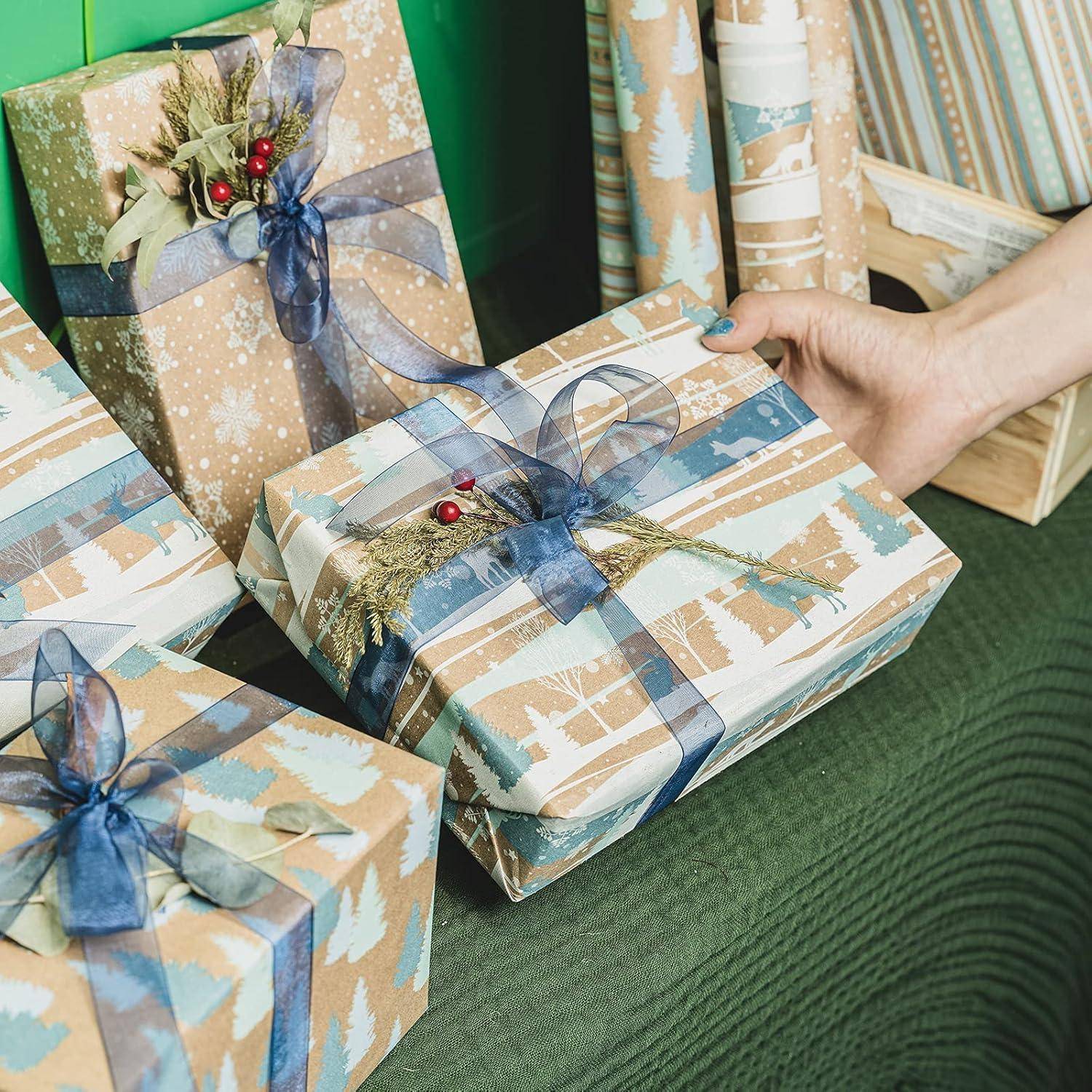 Dekorative Geschenkboxen mit Feiertagsmotiv, in blau-goldenem Geschenkpapier und mit Schleifen, wobei eine Box auf einer grünen Stoffoberfläche platziert ist.