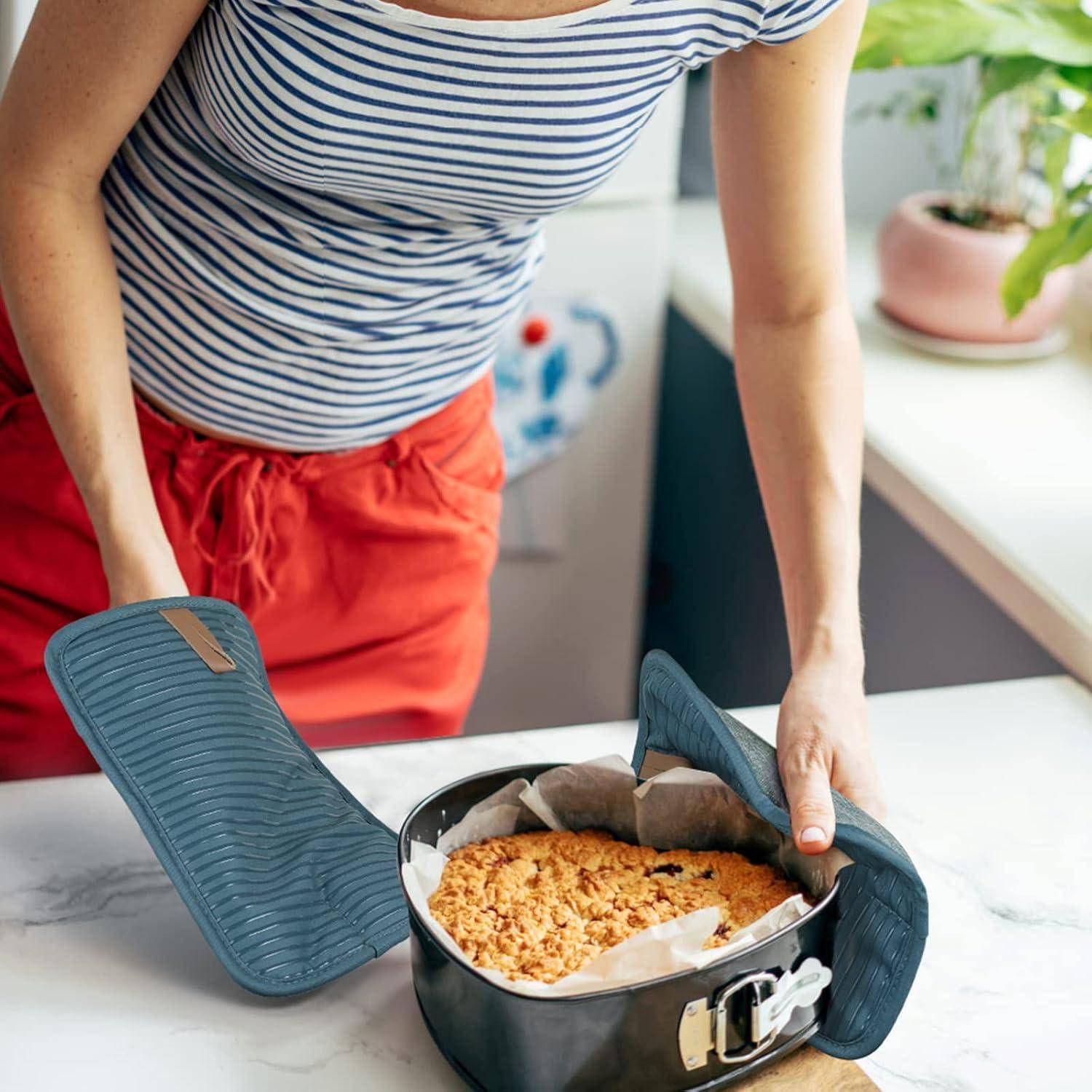 Eine Person in einem gestreiften Hemd und roten Hosen öffnet eine Backform mit einer frisch gebackenen, krümeligen Torte auf der Küchenarbeitsplatte.