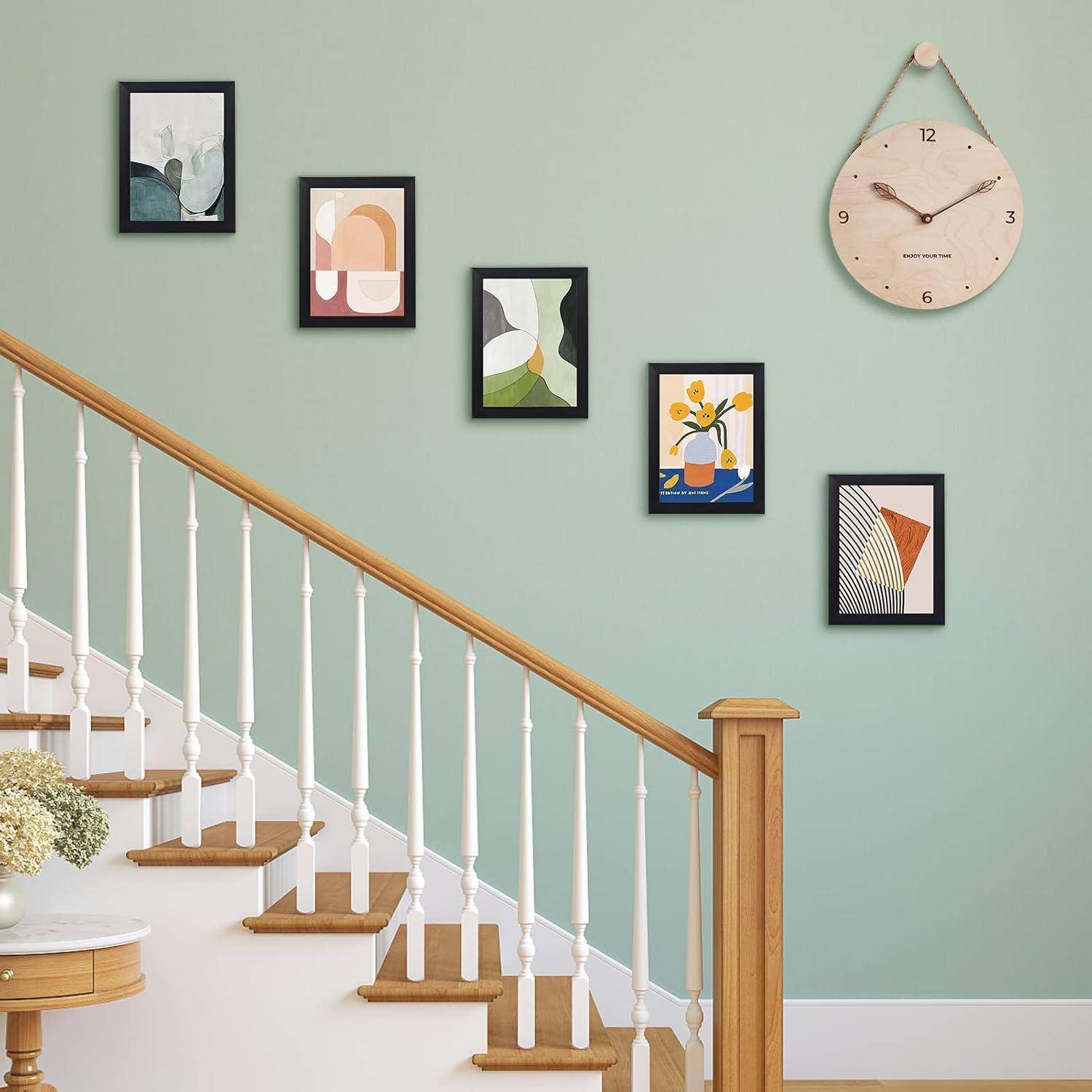 Eine Treppe mit Holzgeländer steigt neben einer mintgrünen Wand empor, die mit fünf abstrakten Kunstrahmen und einer runden Uhr geschmückt ist.